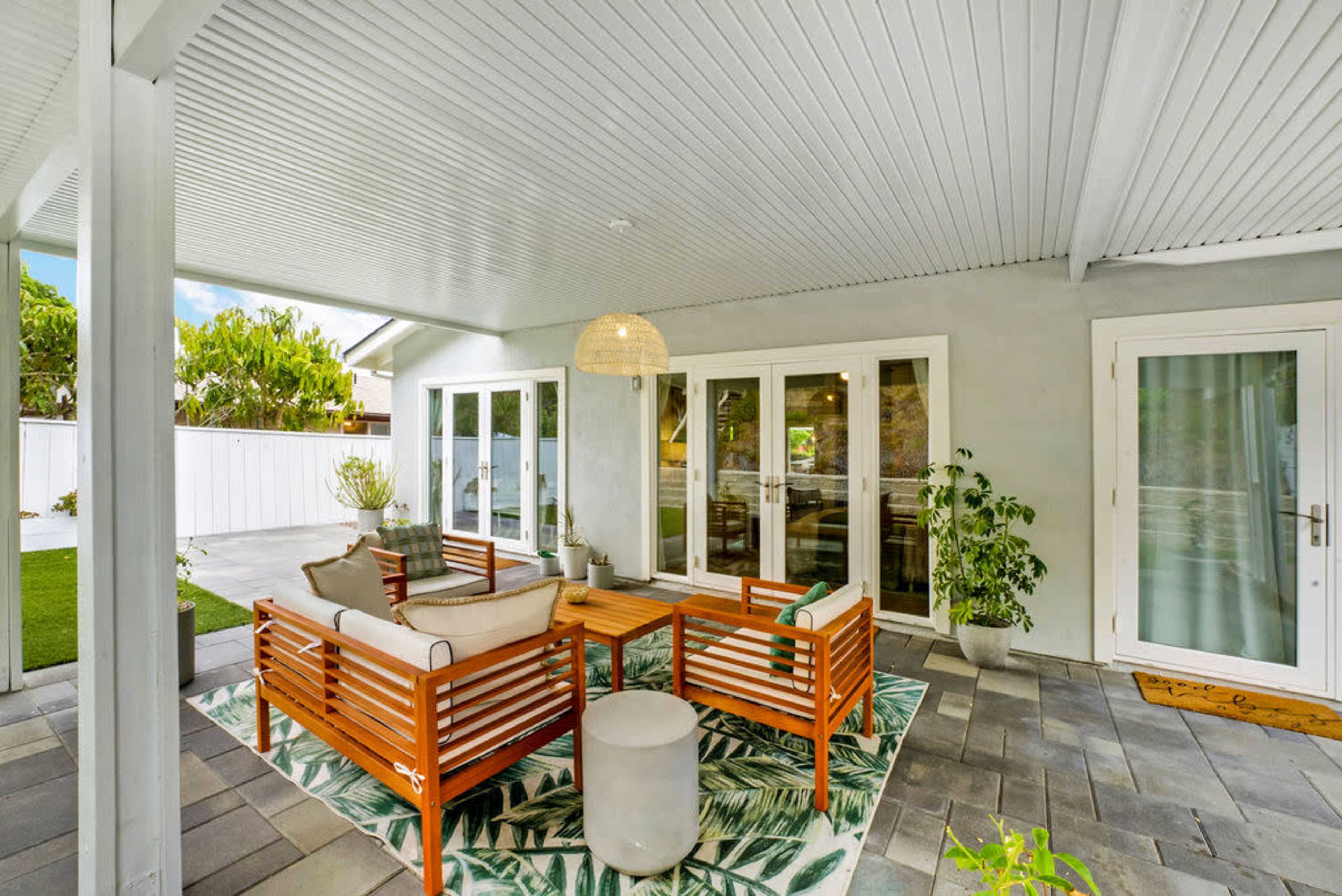 The image shows a covered patio area furnished with a seating arrangement and a decorative light fixture.
