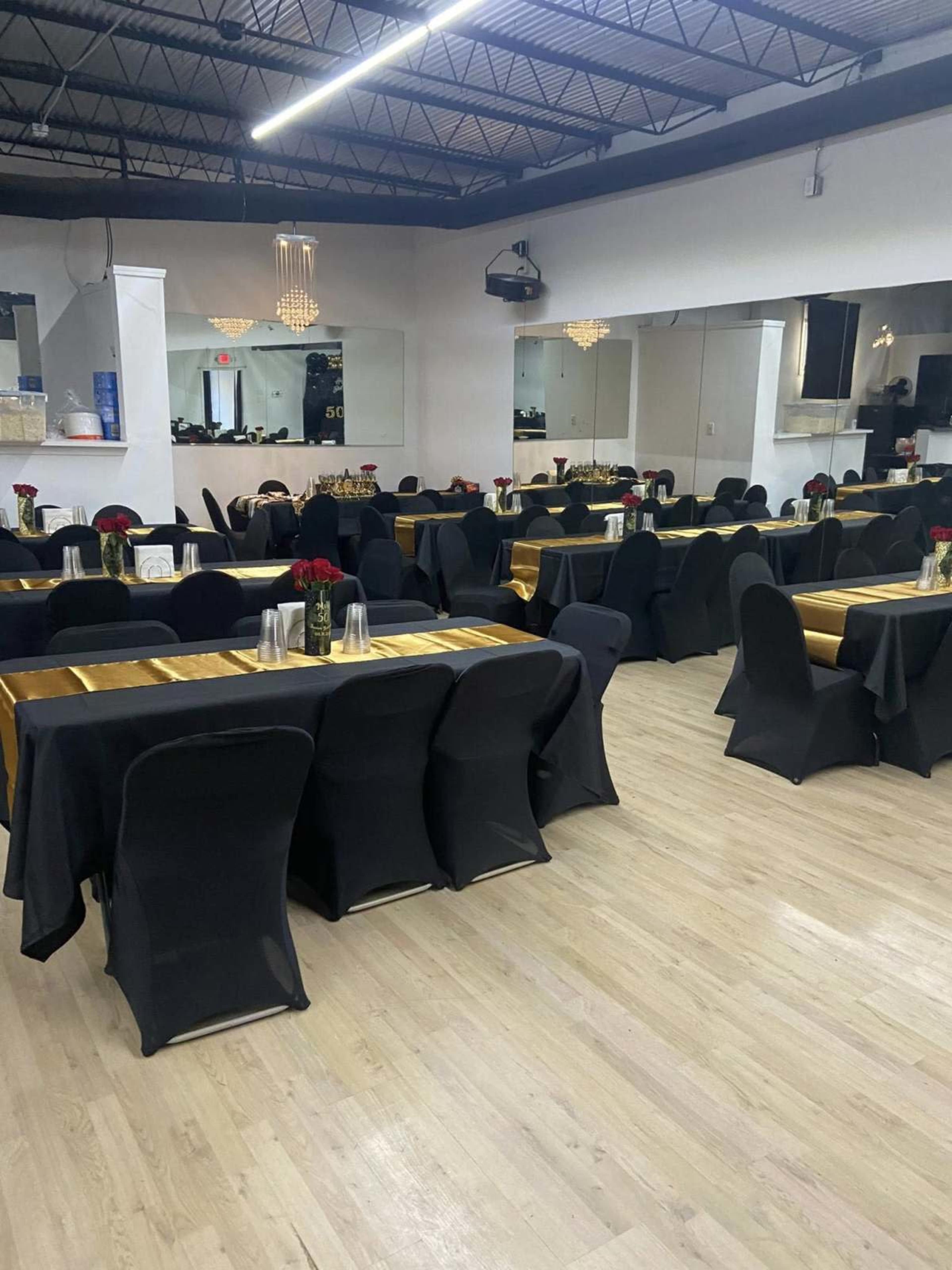 The image shows a dining area with several tables covered in black tablecloths and gold runners, arranged with floral centerpieces.