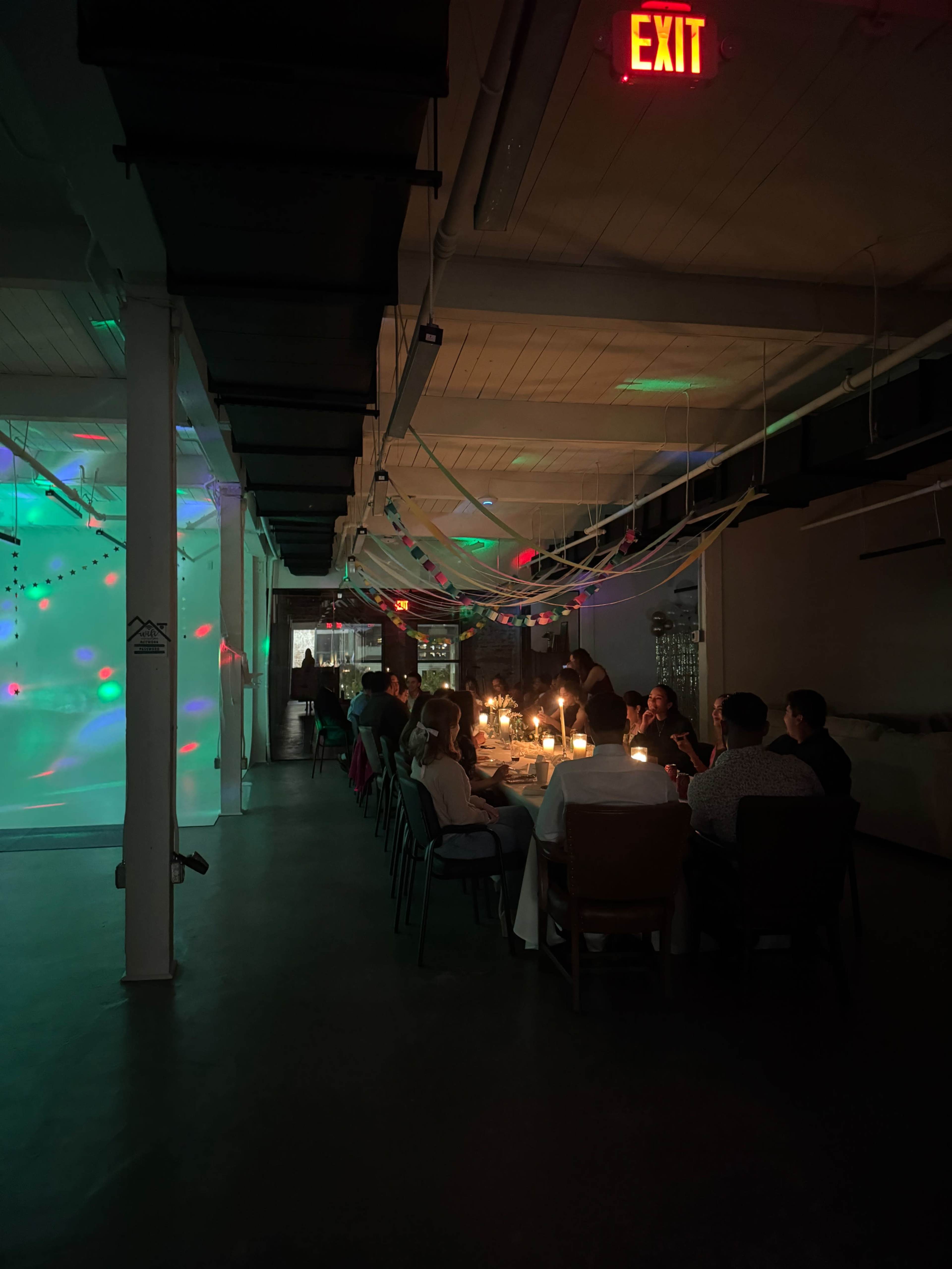A long table with diners is set up under soft lighting, while colorful projections illuminate the walls of a spacious indoor venue.