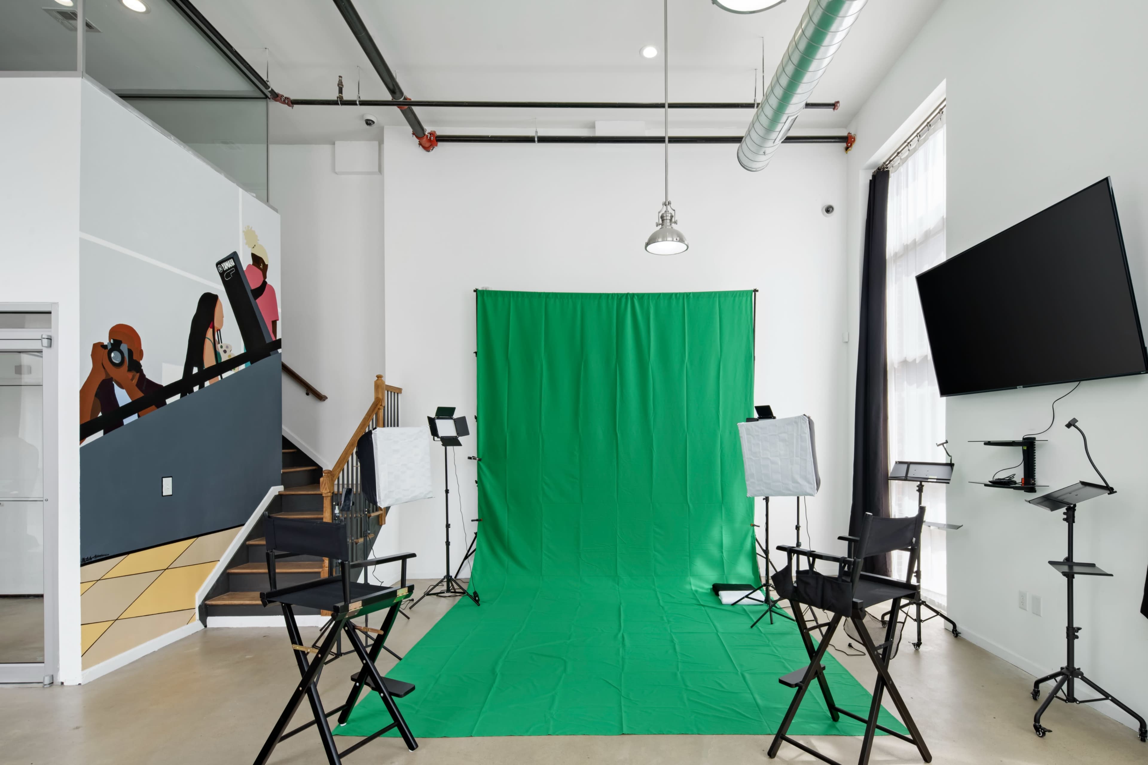 A studio space features a green screen backdrop, two lighting setups, and black director's chairs arranged in front of it.
