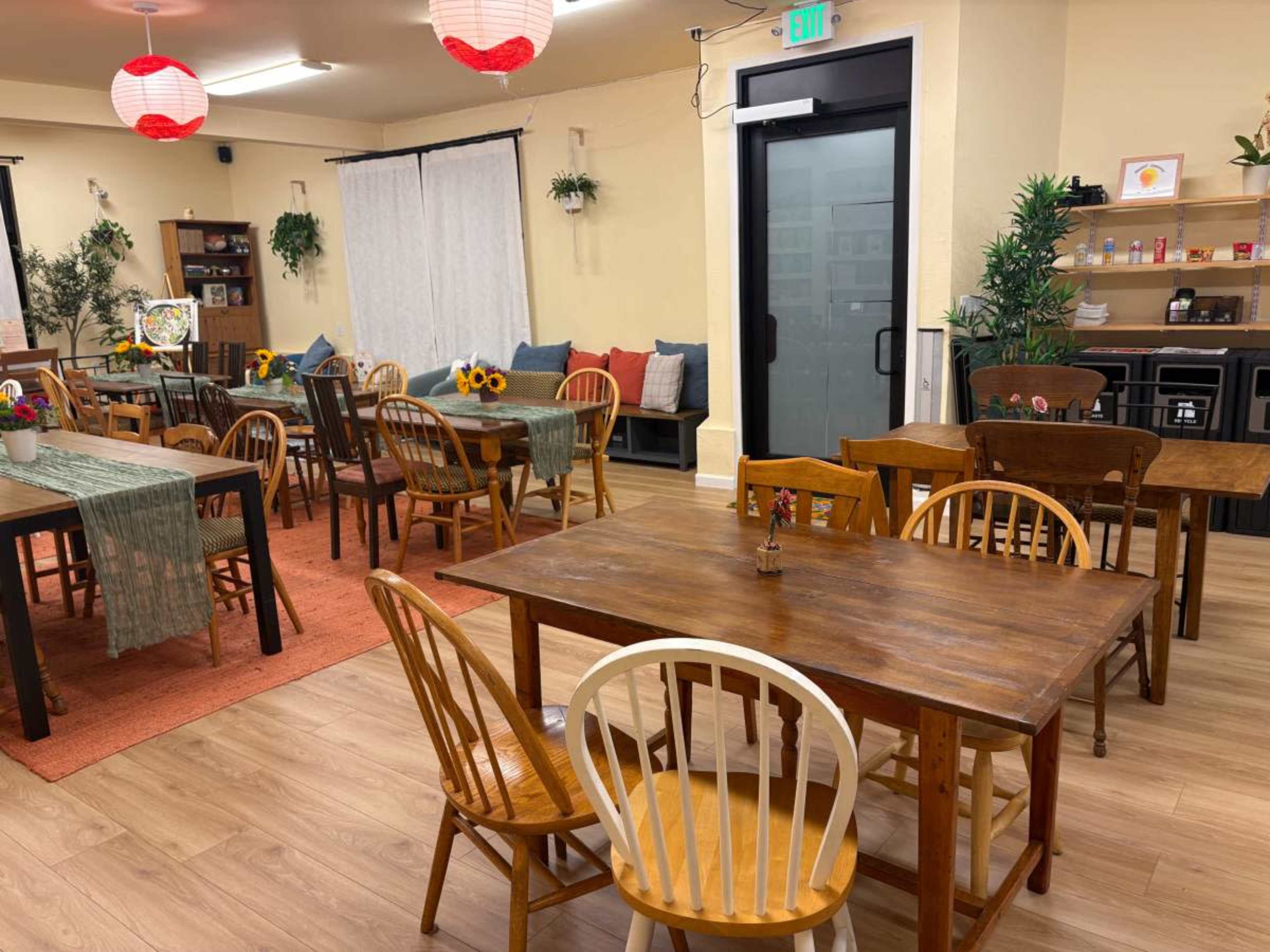 The room features a layout of wooden tables and chairs, with decorative plants and colorful lanterns hanging from the ceiling.