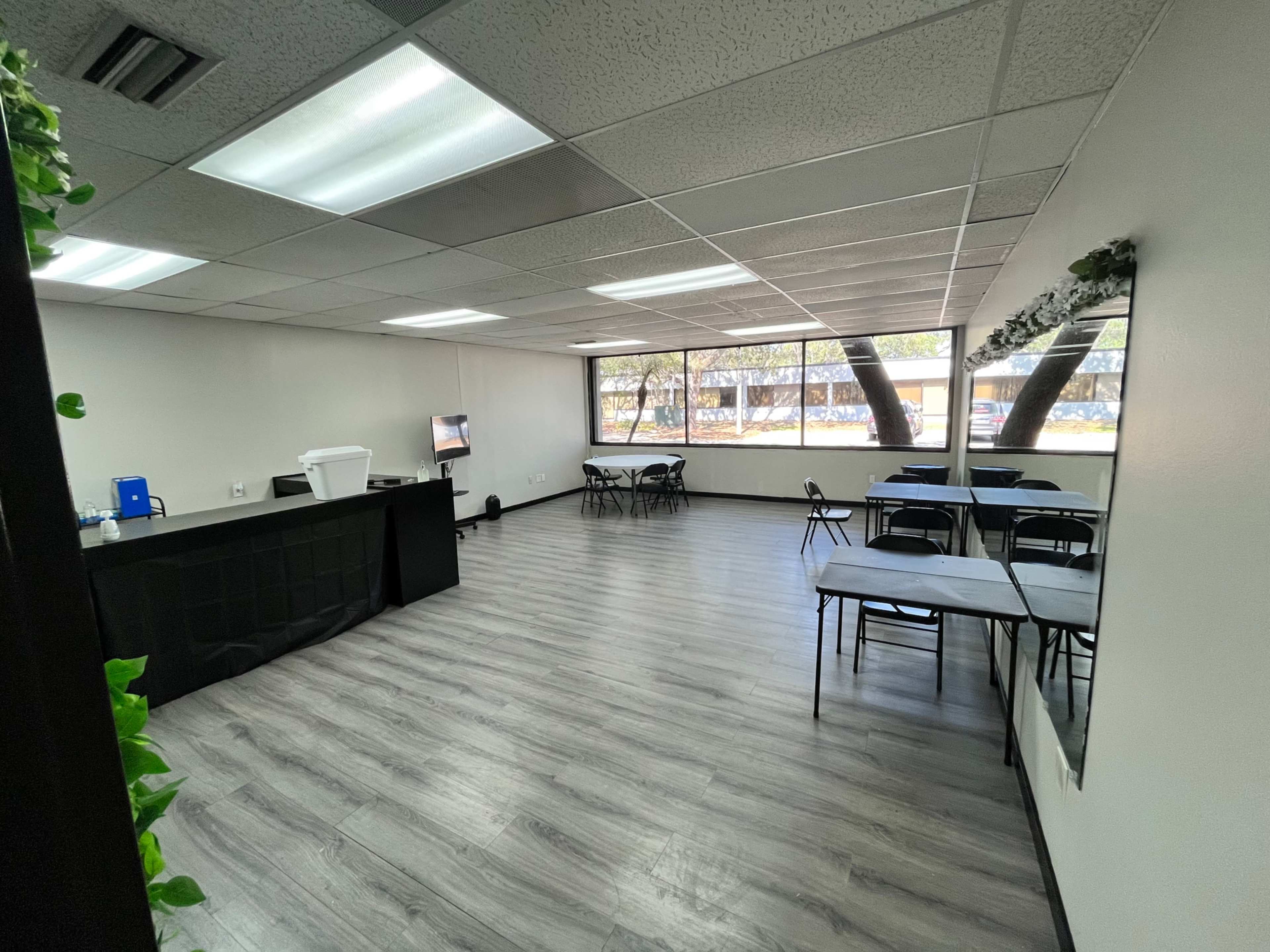An empty room with a bar counter, several tables and chairs, and large windows allowing natural light.
