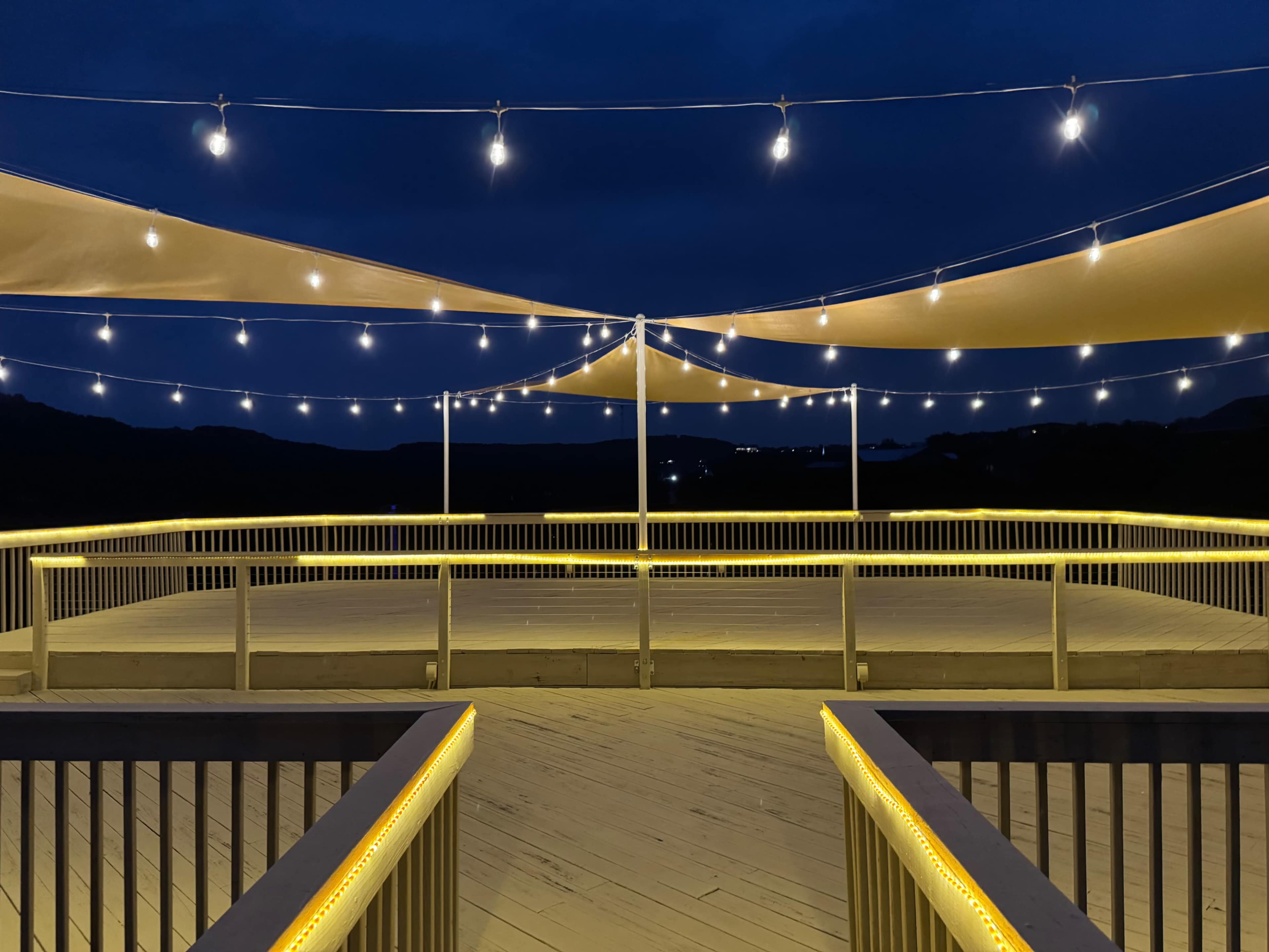 The image shows a wooden deck illuminated by string lights and a tent canopy against a dark evening sky.