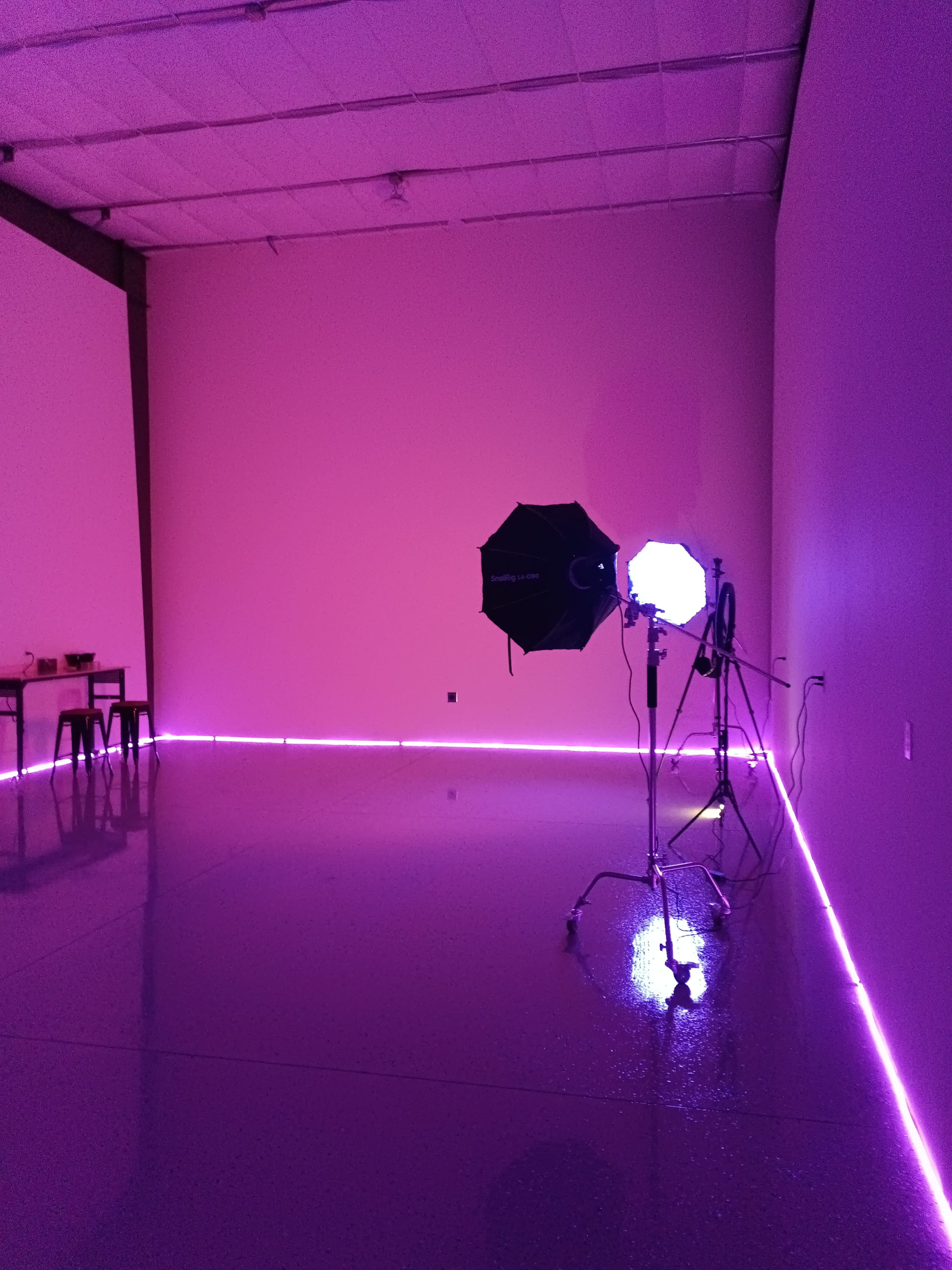 The image shows a minimalistic room with a glossy floor, pink walls, and studio lighting equipment positioned in one corner.