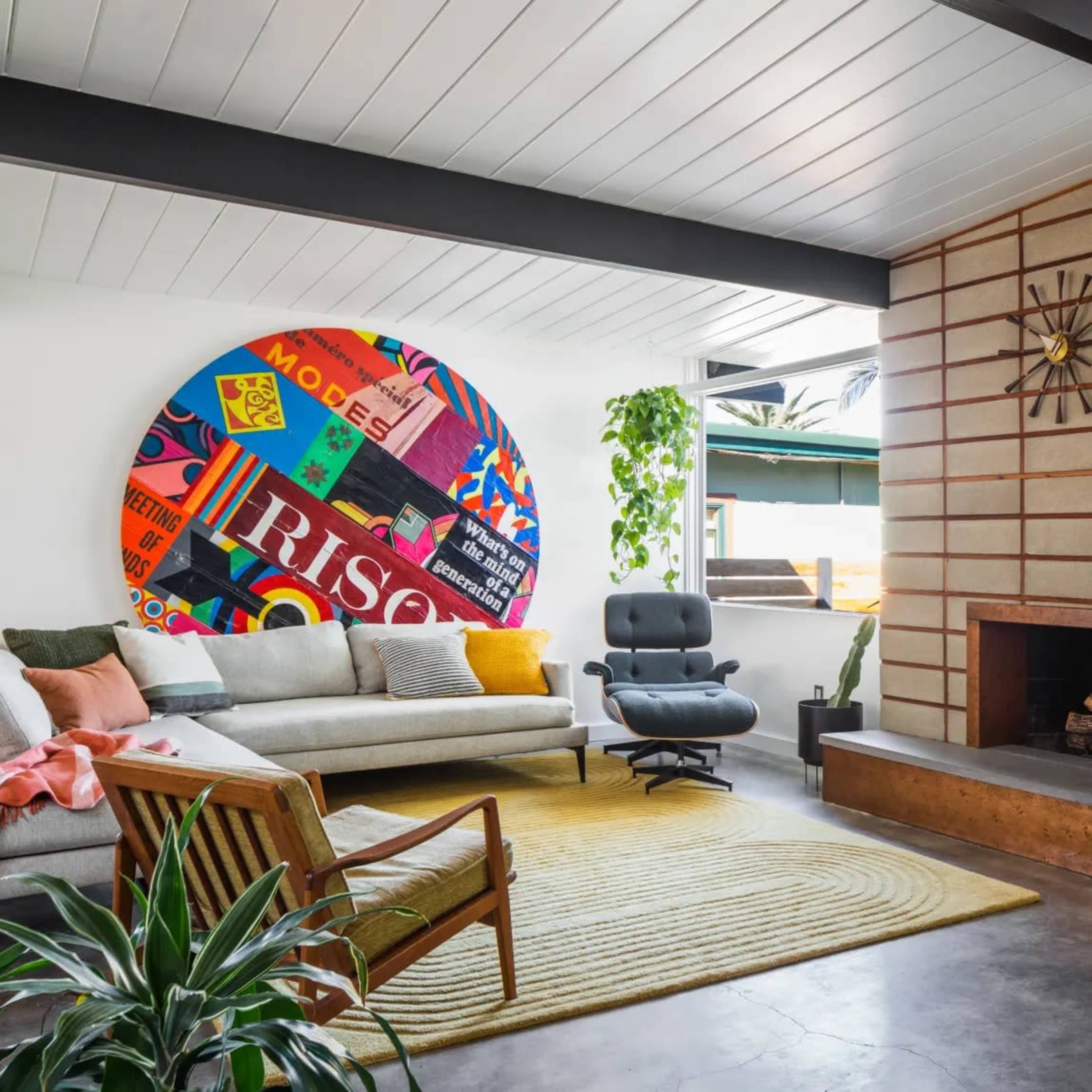 The living room features a large colorful mural, a beige sofa, an armchair, a yellow area rug, and a fireplace against a mid-century modern design backdrop.