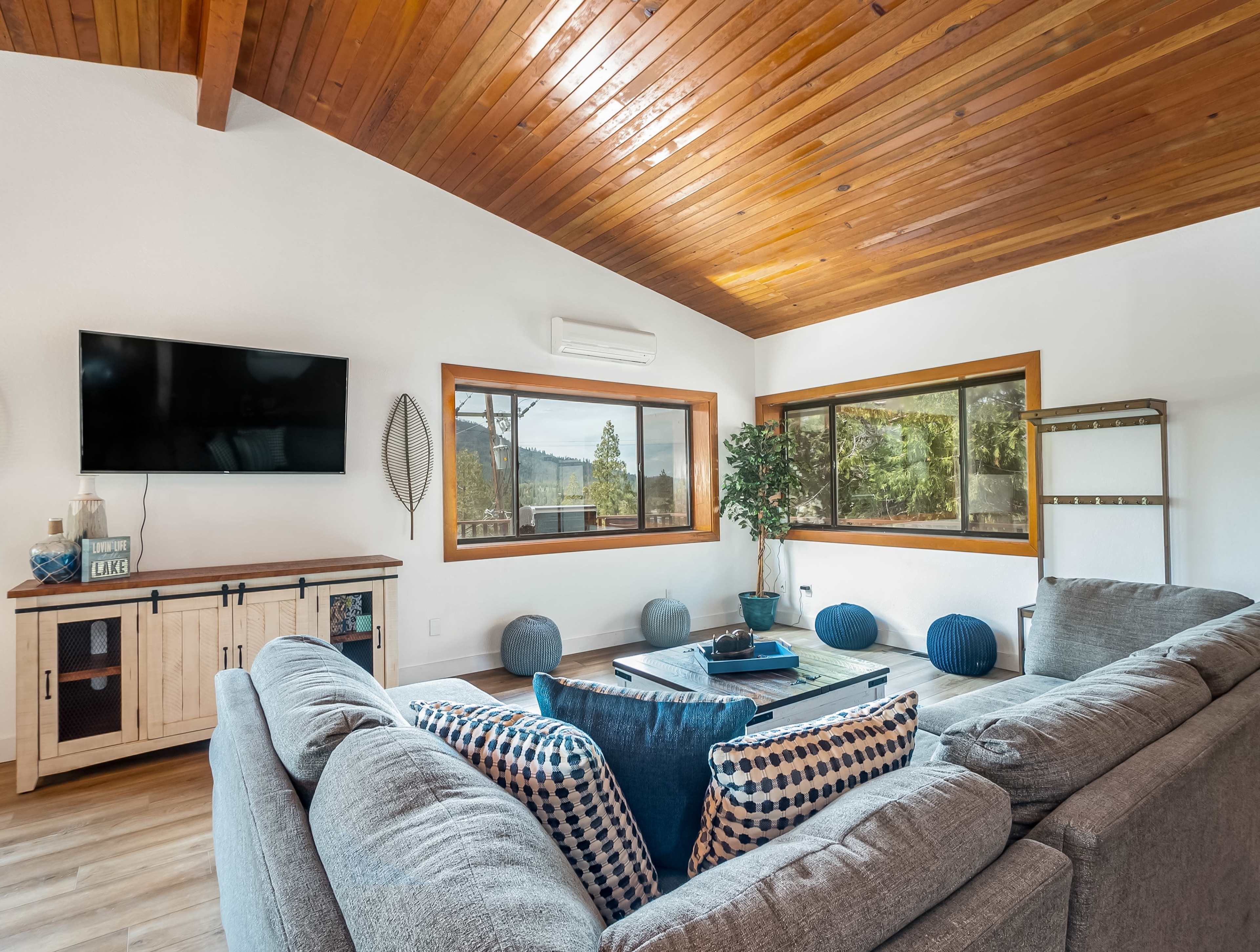 A spacious living room features a gray sectional sofa, a wooden coffee table, and large windows that provide natural light and views of the outdoors.