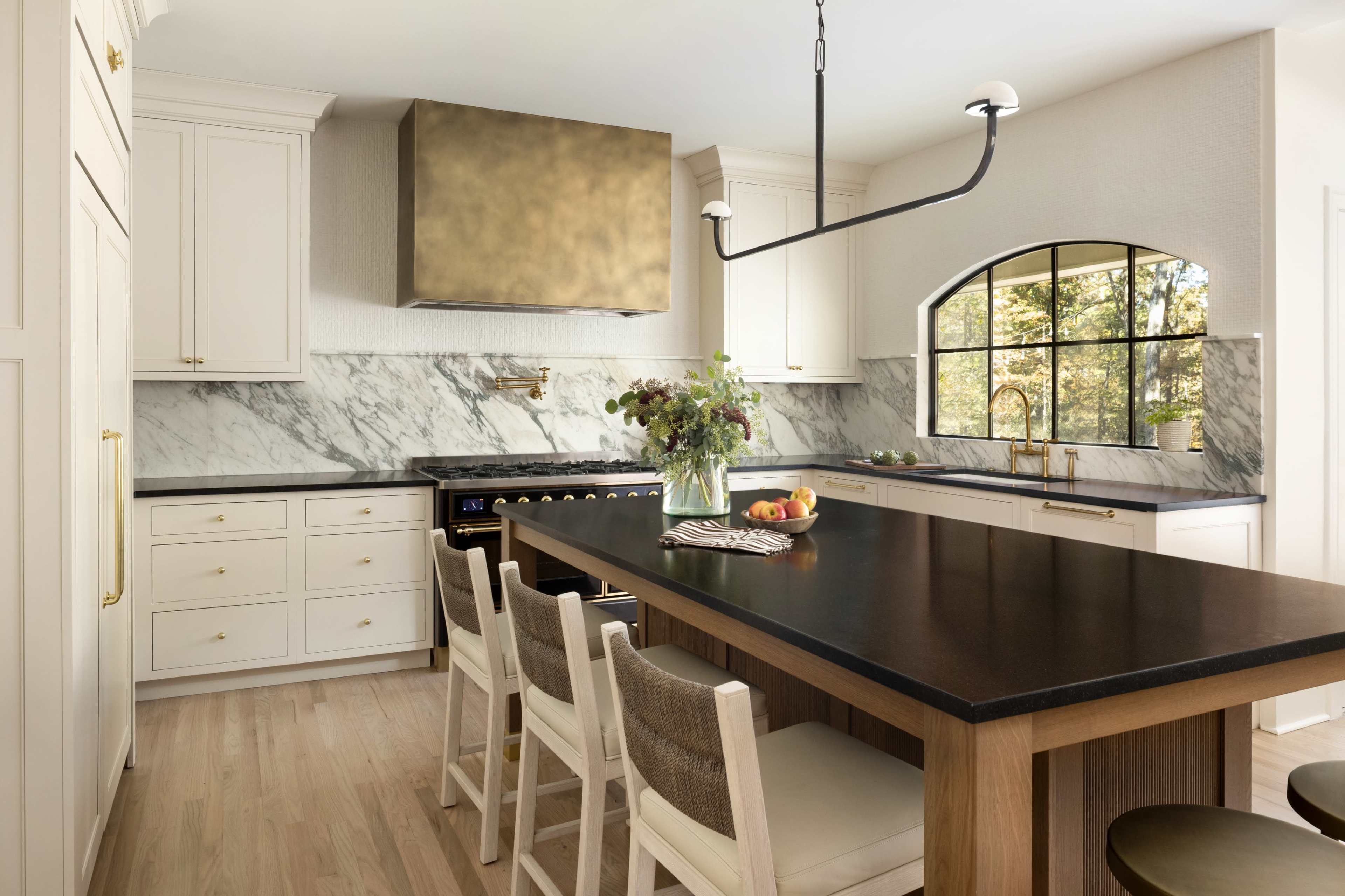The image shows a modern kitchen with marble countertops, a large island with seating, and a sleek range hood above a stove.