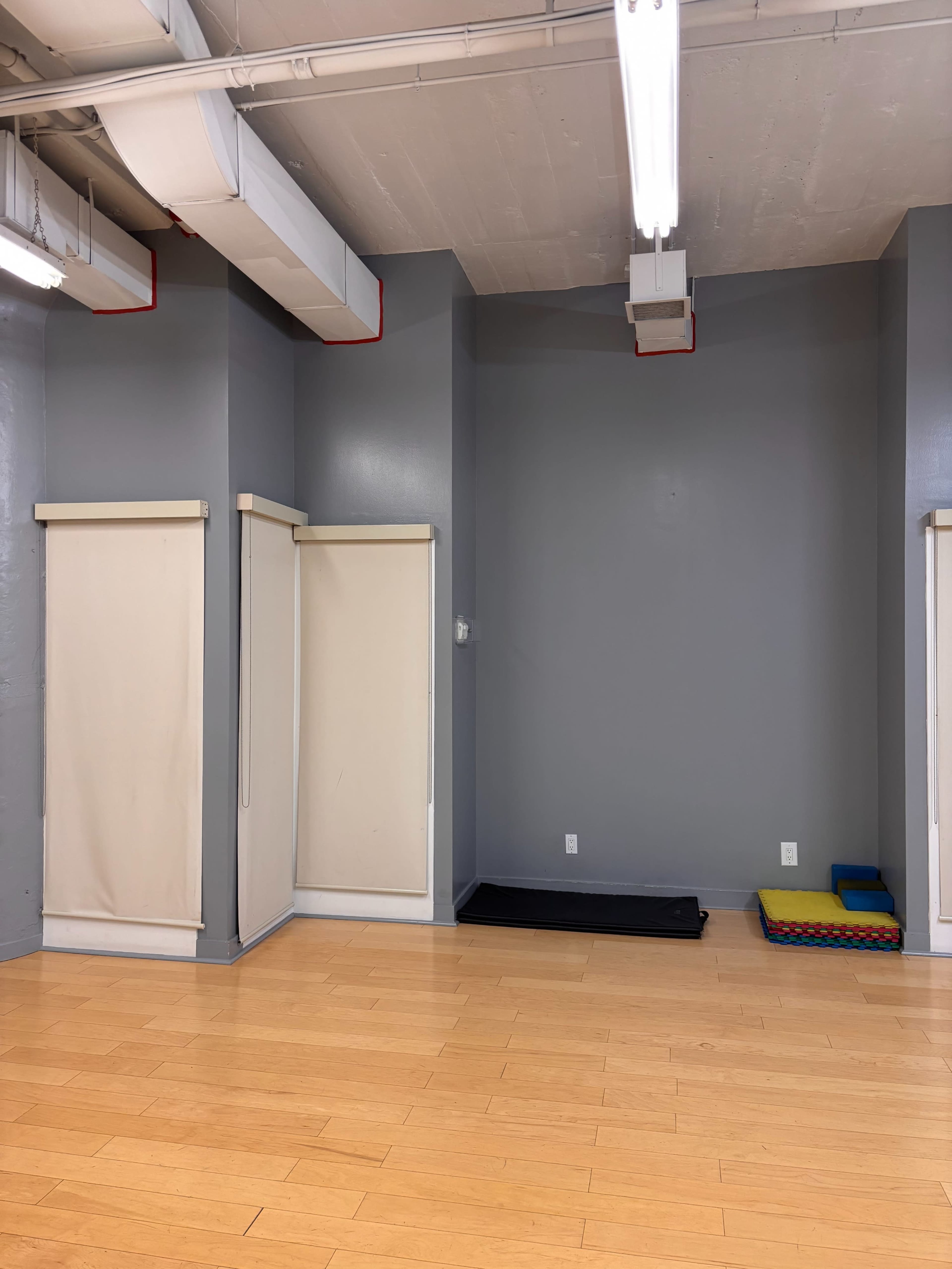 The image shows a spacious room with light wooden flooring, gray walls, and two beige wall-mounted folding partitions.