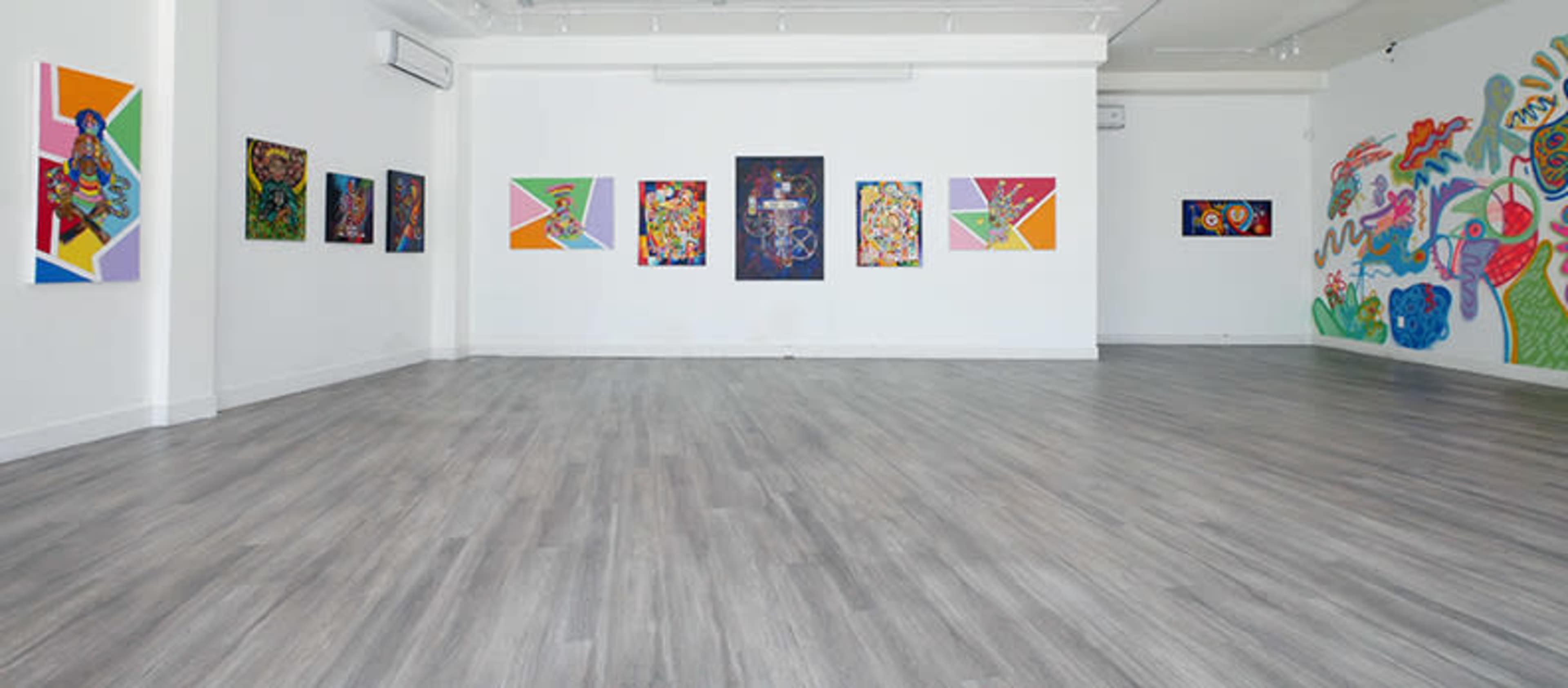 An art gallery featuring colorful paintings displayed on white walls, with a spacious wooden floor.