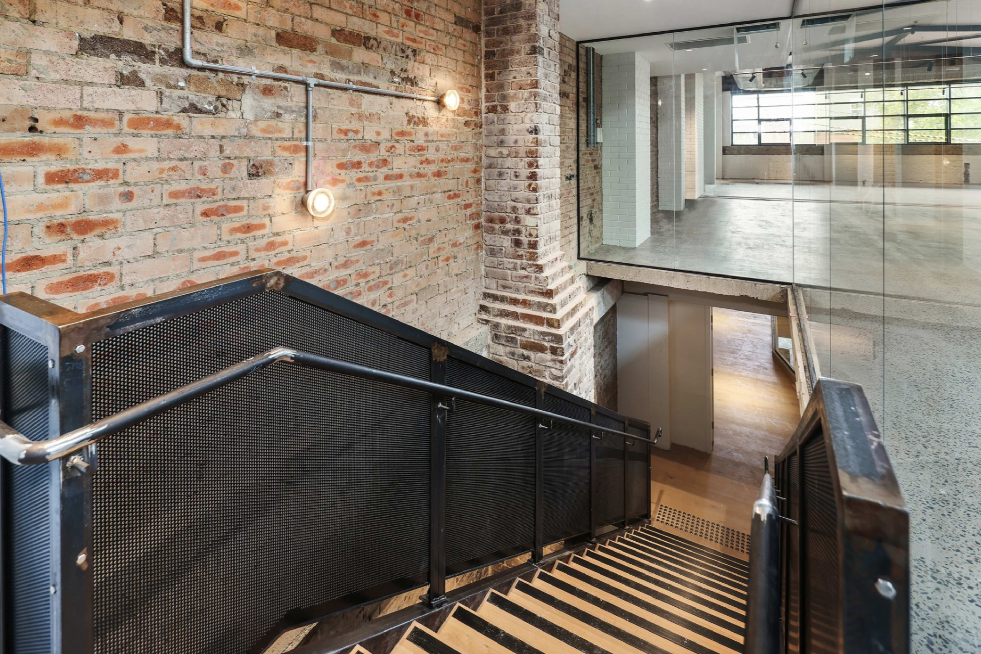 A staircase made of wood and metal descending from a brick-walled area into a spacious room with large windows.