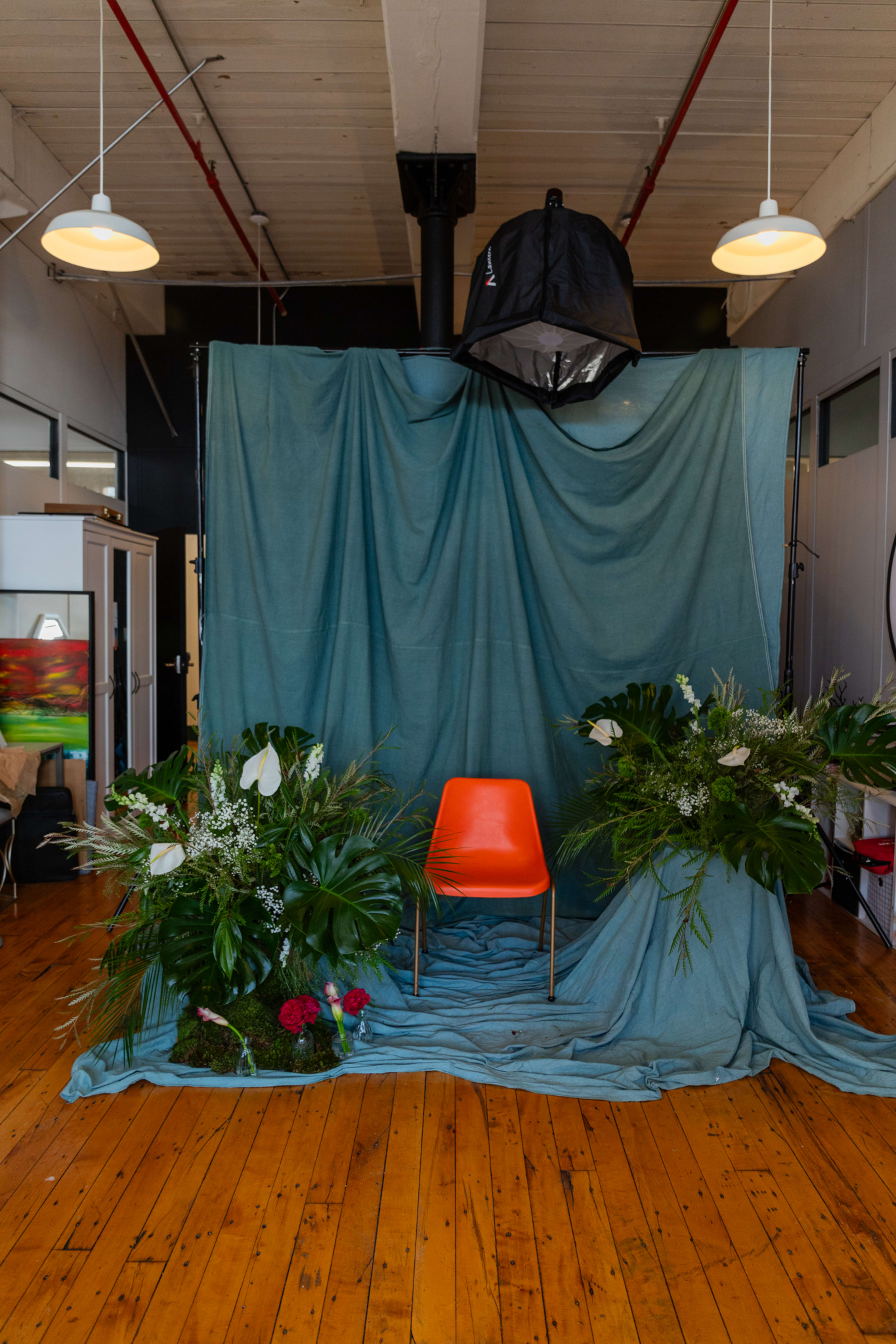 A bright orange chair sits in front of a blue backdrop adorned with tropical plants and flowers in a spacious indoor setting.