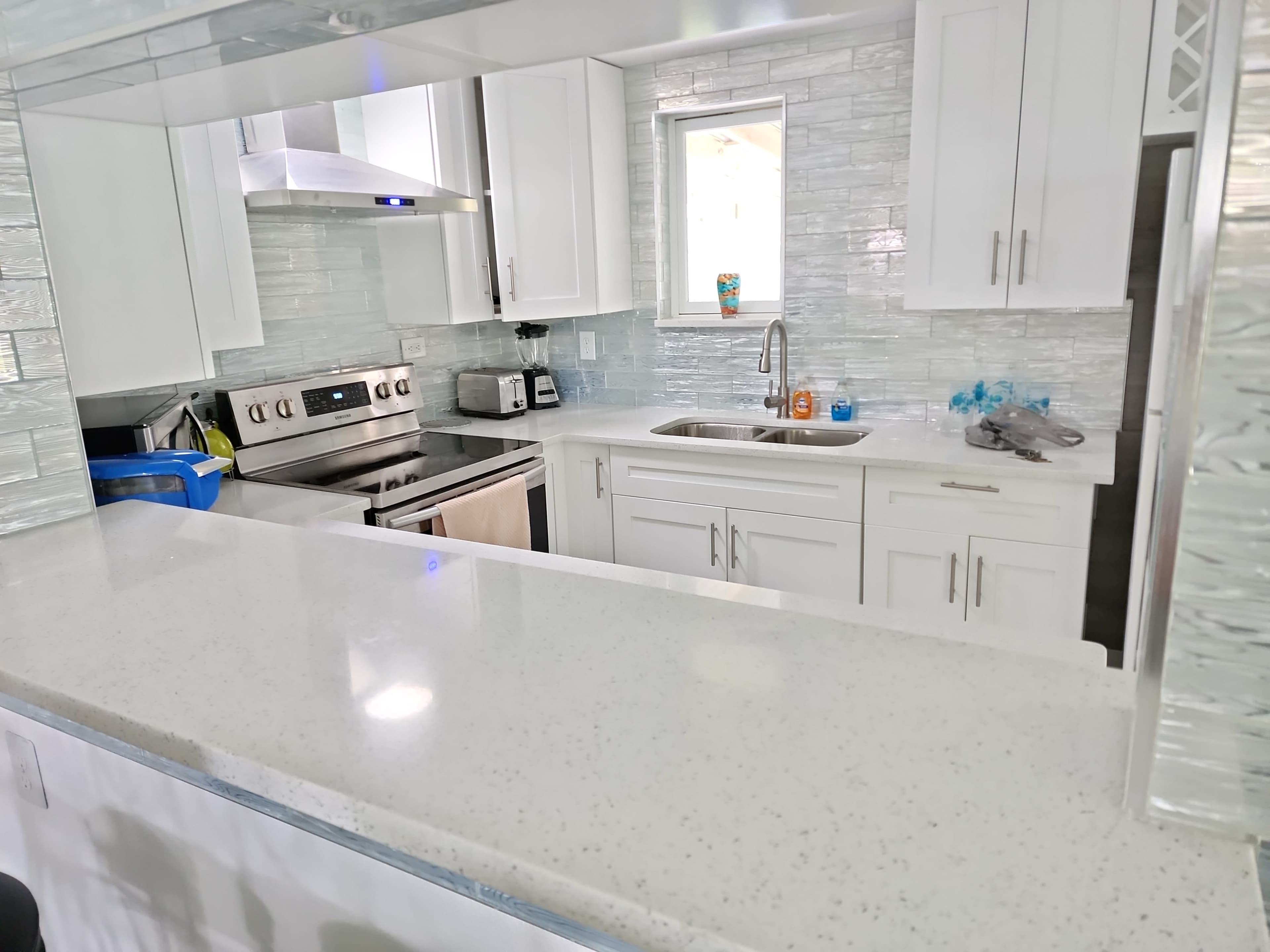 A modern kitchen with white cabinets, a stainless steel stove, and a countertop made of light-colored material.