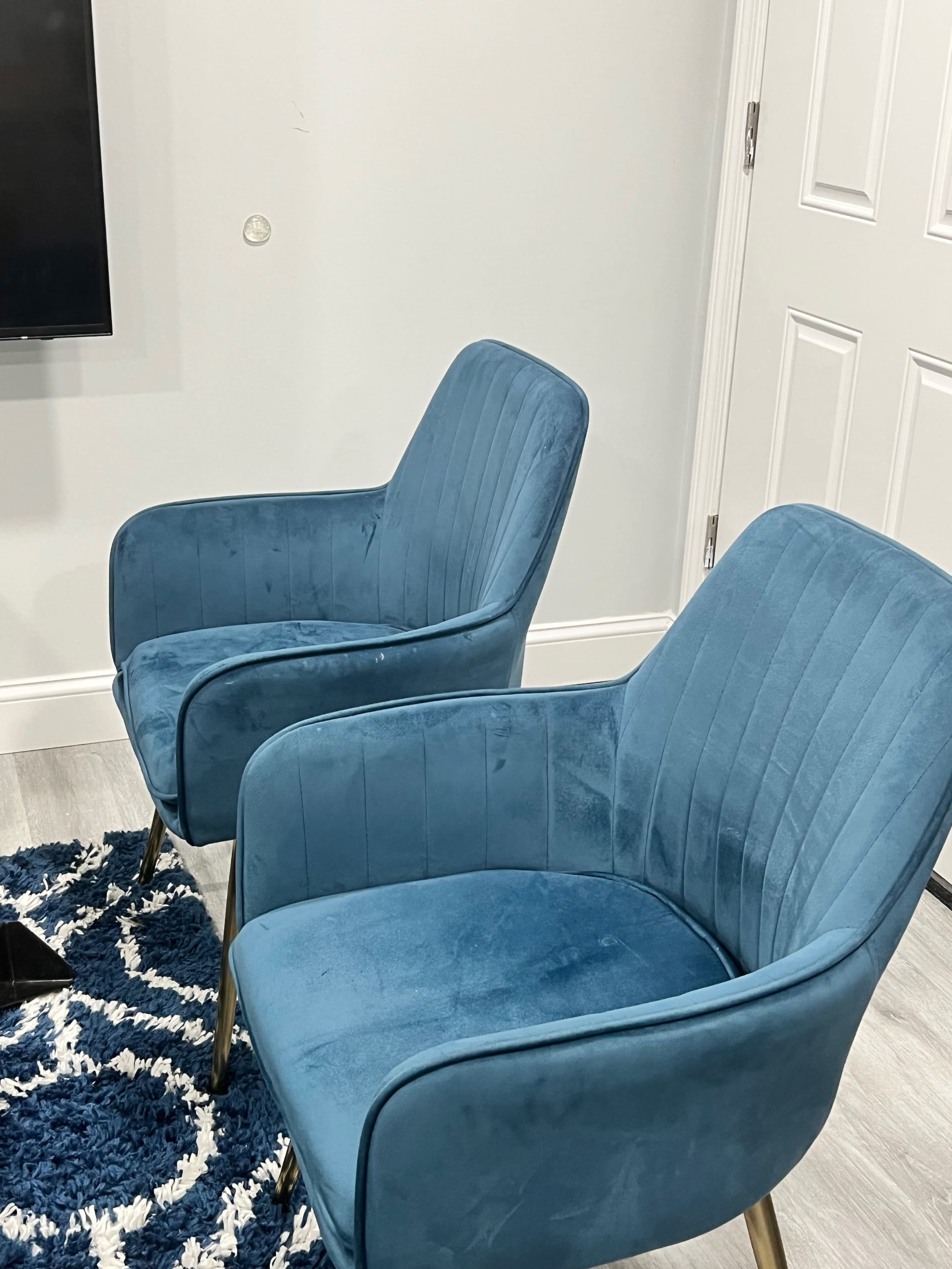 Two blue upholstered chairs with gold legs are positioned on a patterned rug in a room with light-colored walls.