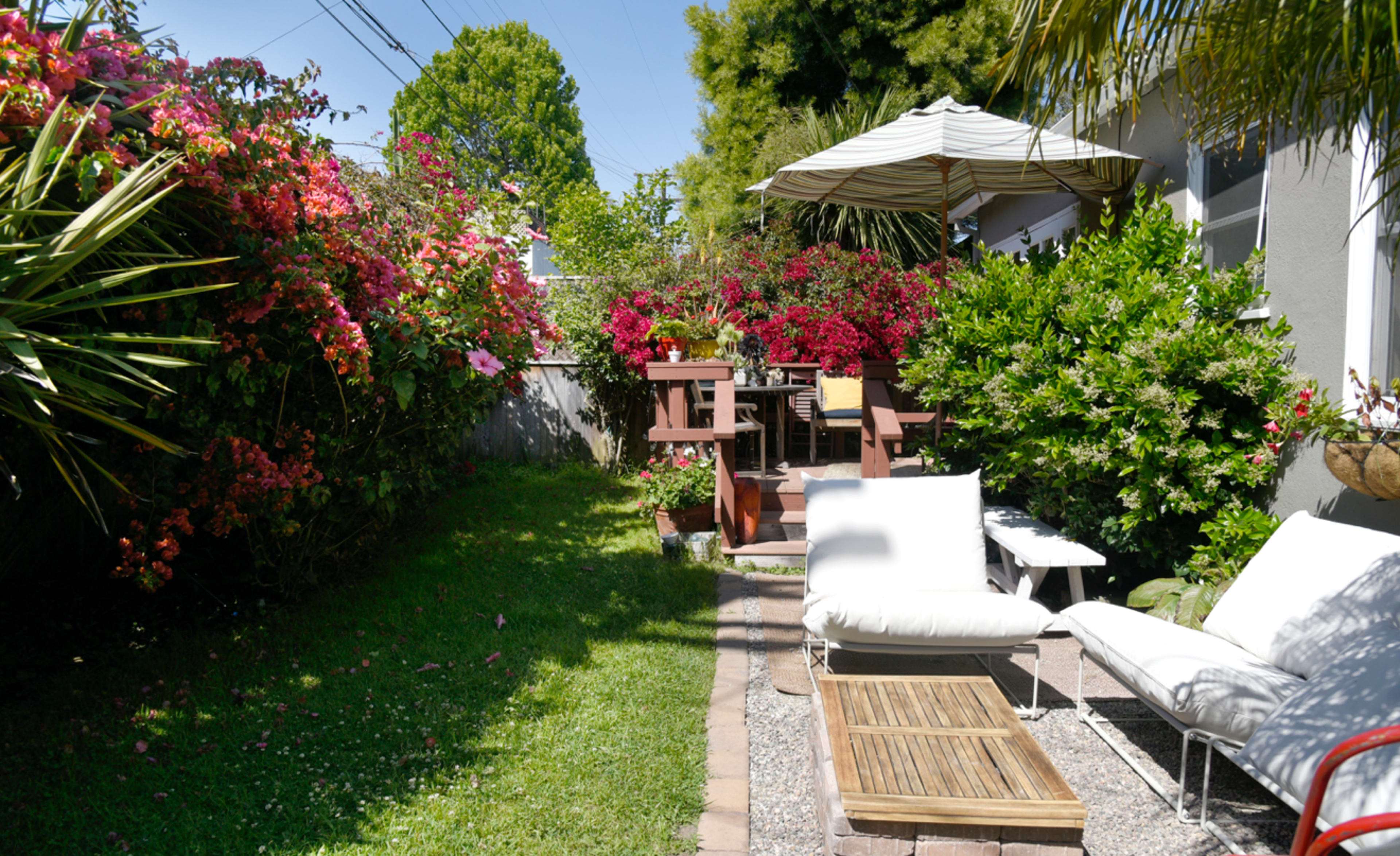 A well-maintained garden features a pathway lined with gravel, leading to seating areas surrounded by vibrant flowers and greenery.