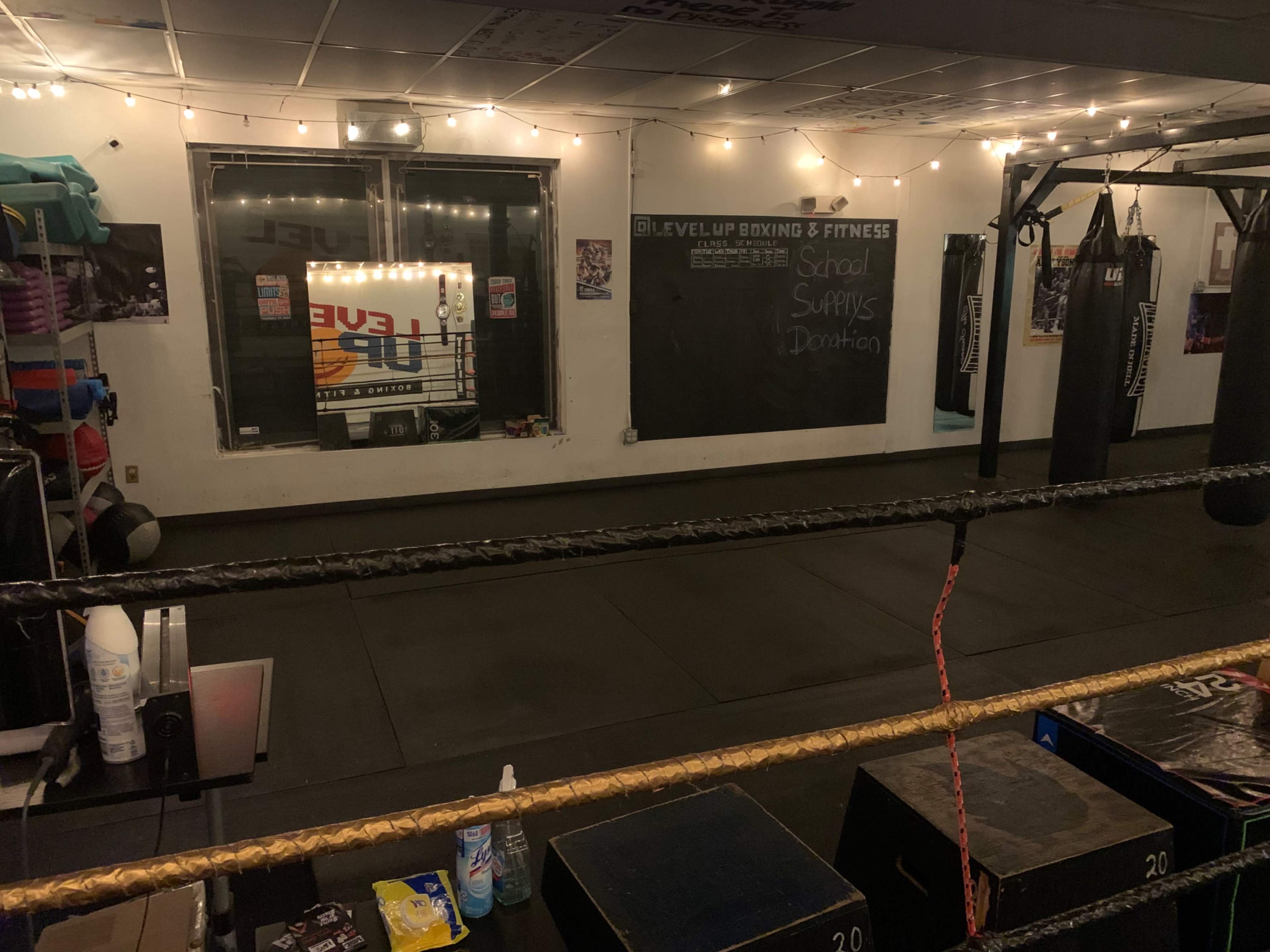 A boxing gym featuring punching bags, a boxing ring, and a chalkboard with information about school supplies and donations.
