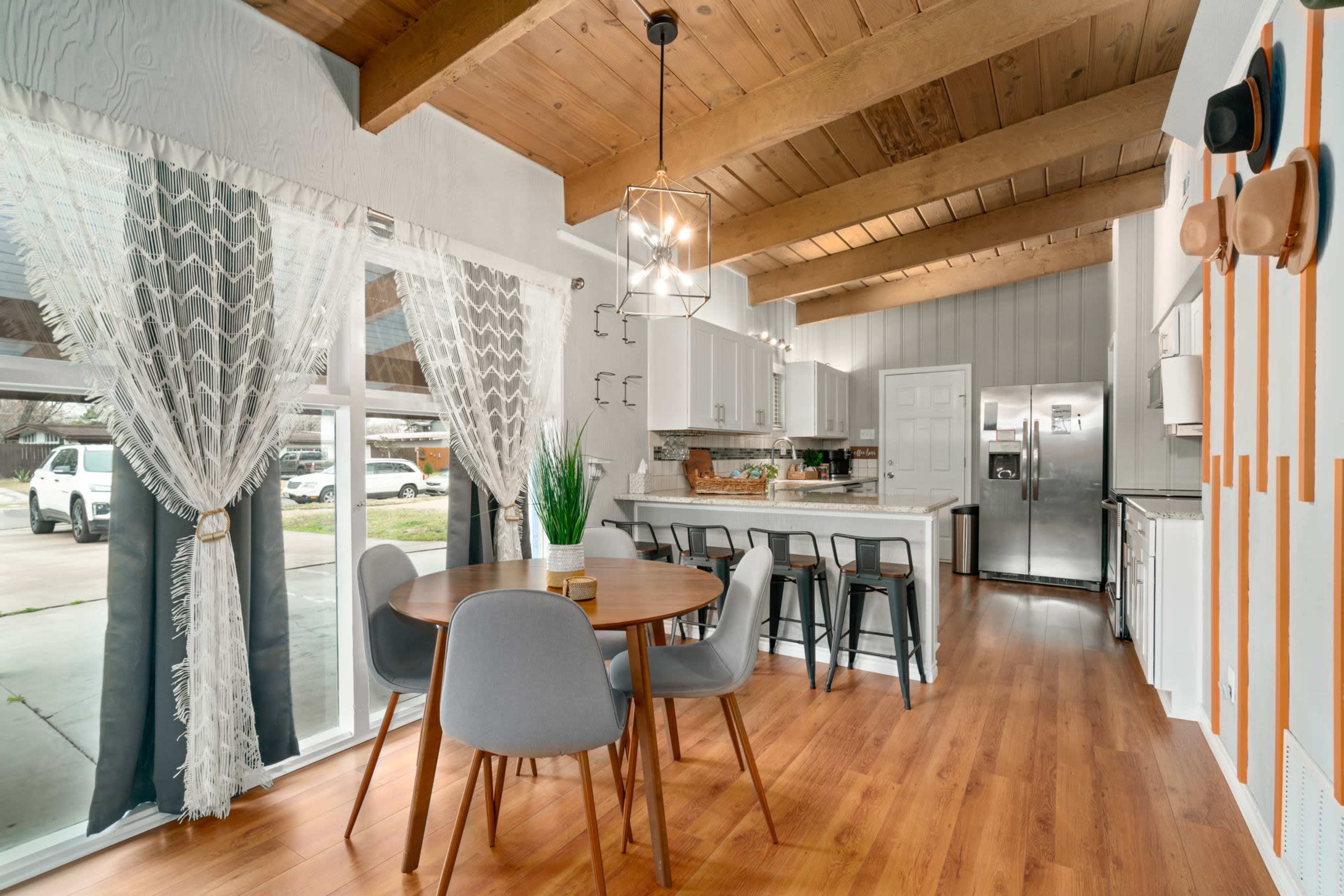 A modern kitchen and dining area featuring a round table with gray chairs, large windows, and wood-beamed ceilings.