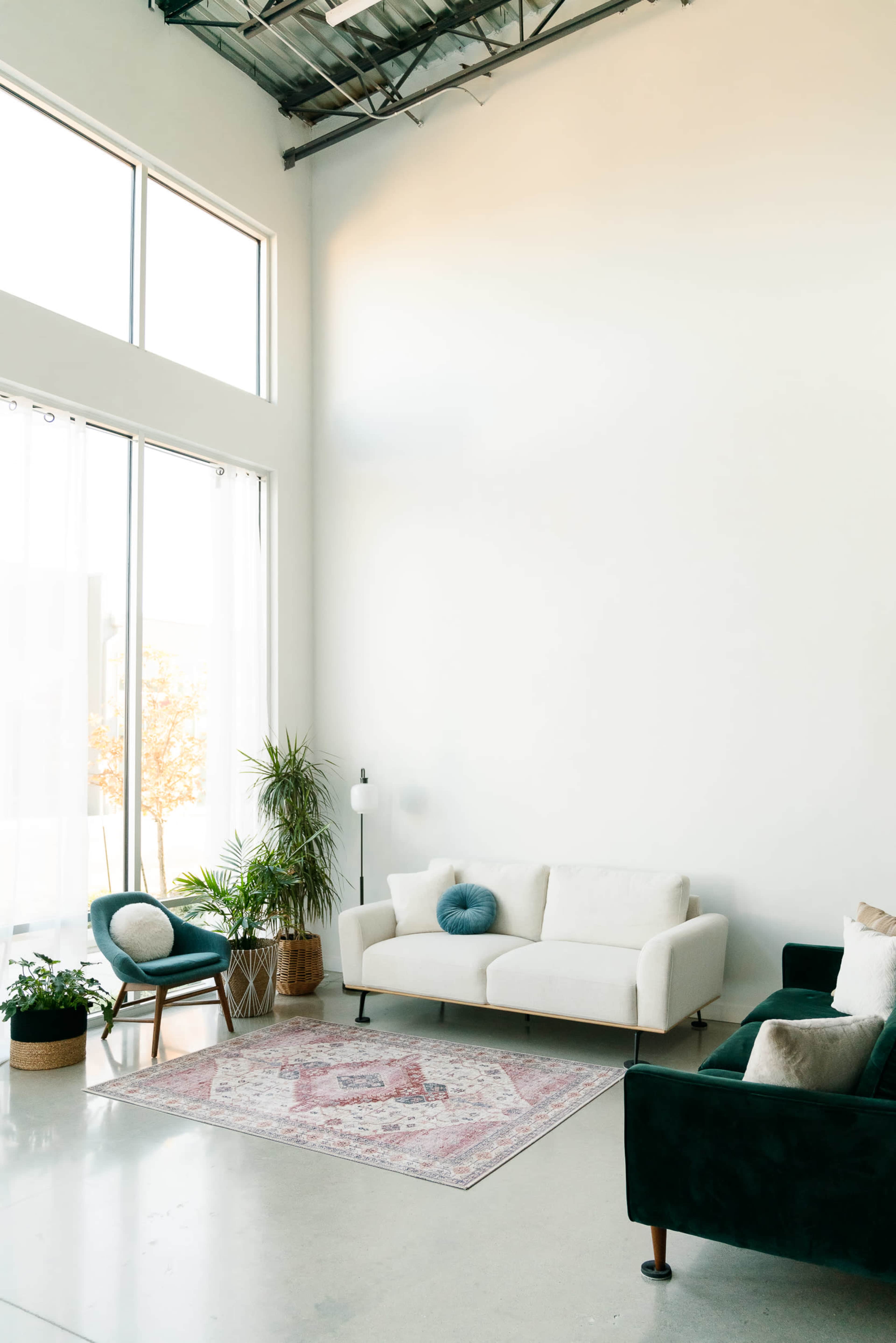 A modern living room featuring a white sofa, a green armchair, a decorative rug, and large windows allowing natural light to enter.