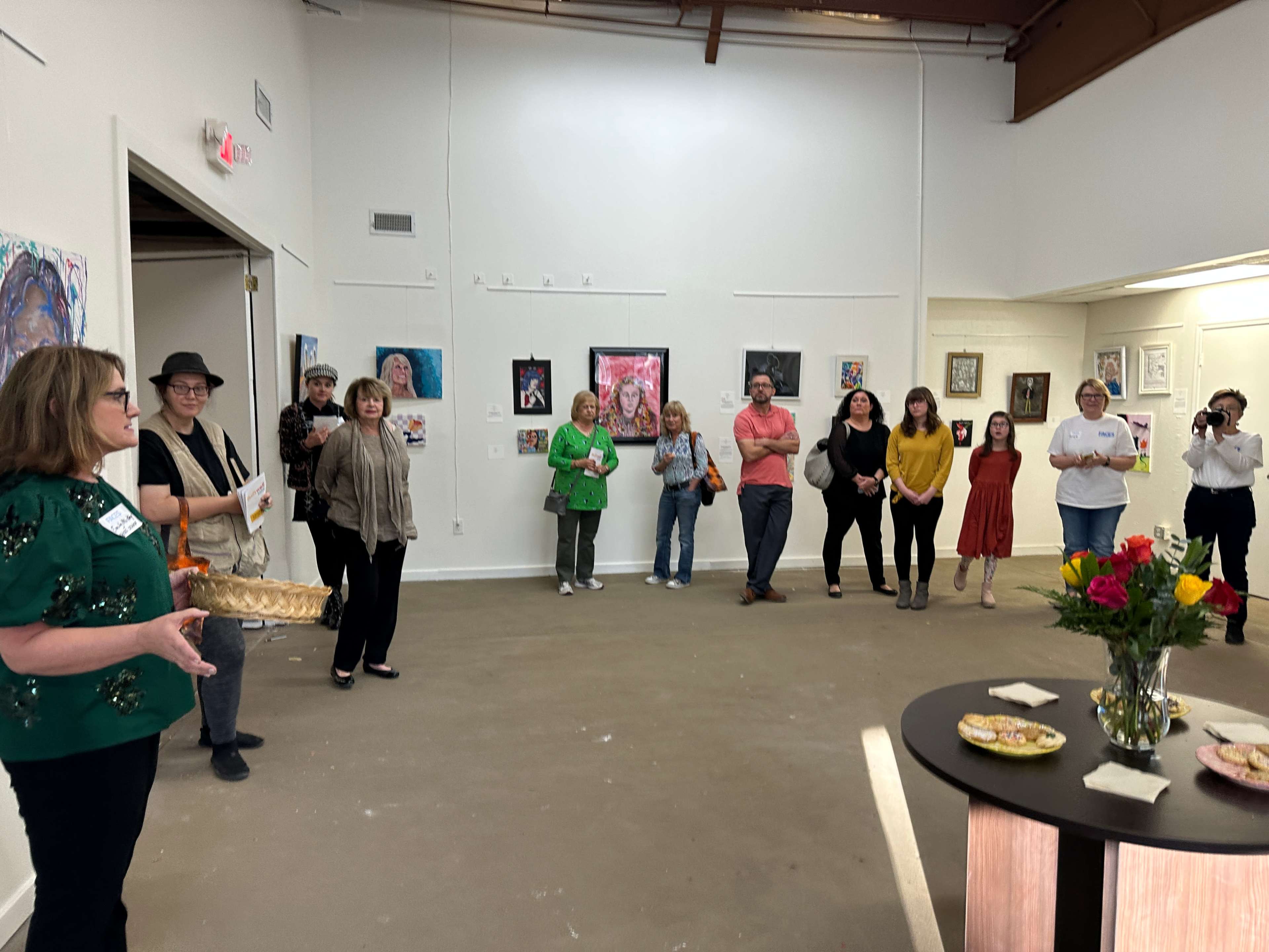 A group of people gathers in an art gallery, with artworks displayed on the walls while one person speaks to the audience.
