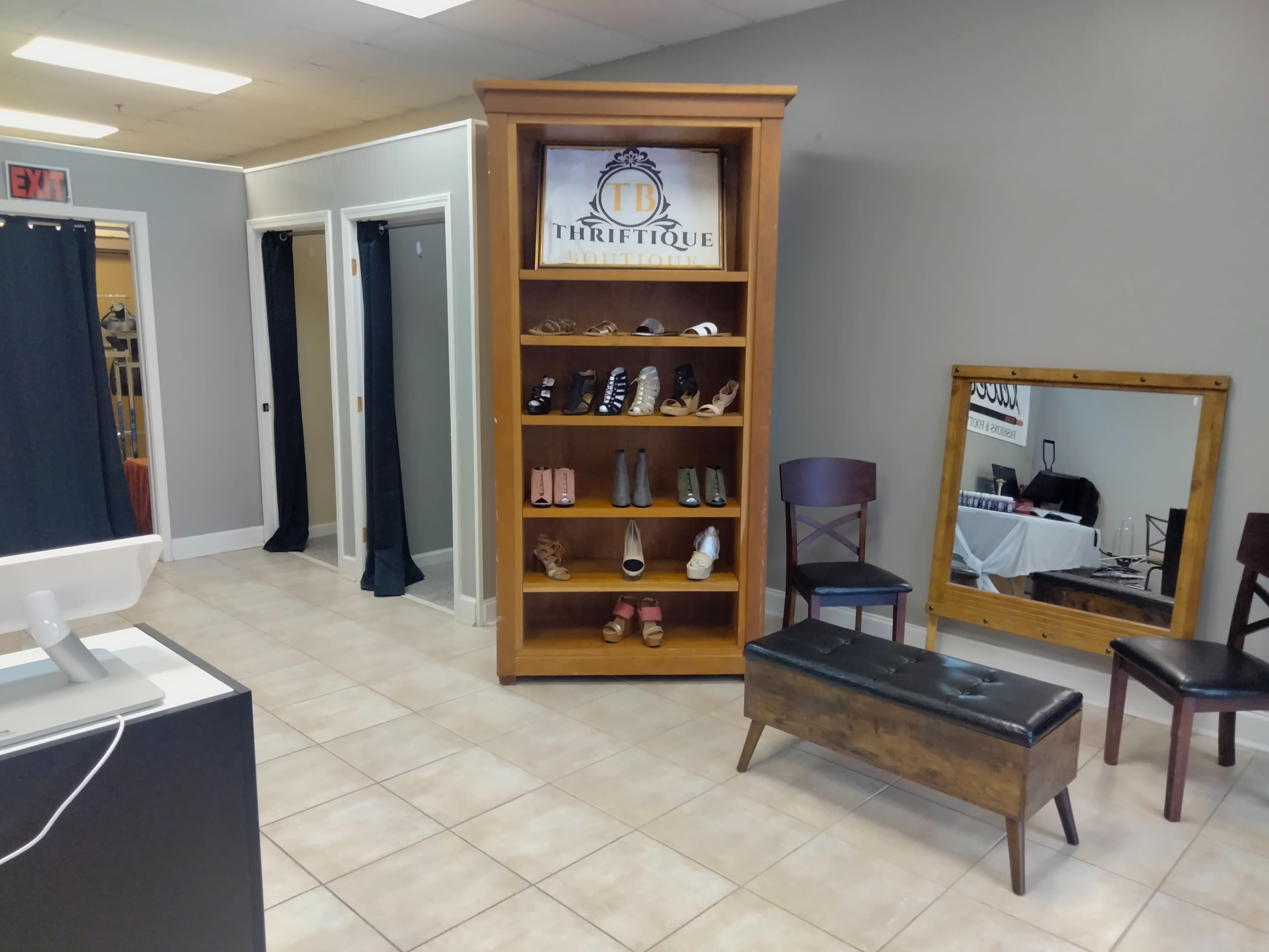 A wooden display shelf with shoes, situated in a retail space featuring gray walls and tiled flooring, with changing areas in the background.