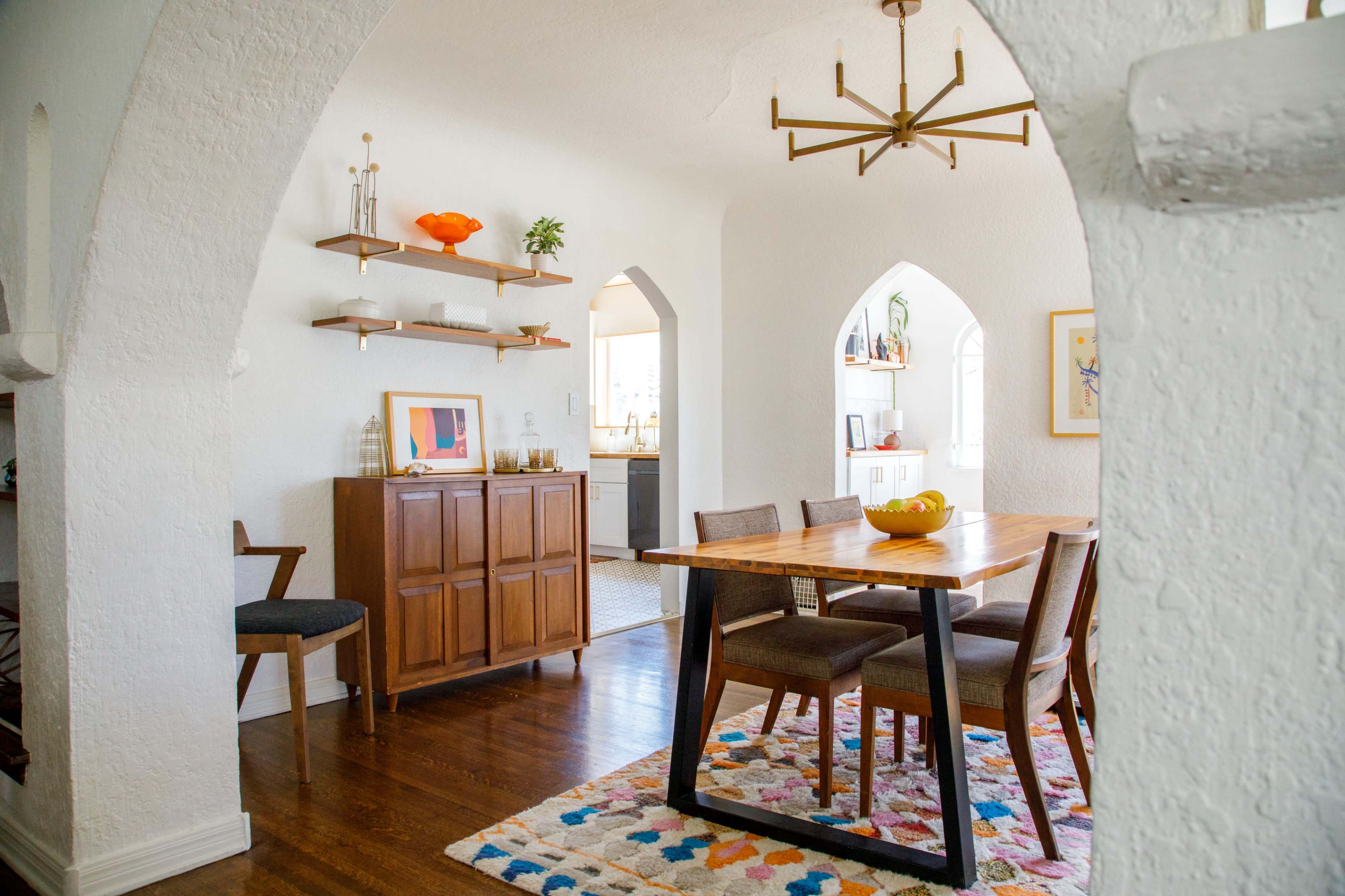 A dining area featuring a wooden table with four chairs, a decorative rug, a sideboard, and archways leading to adjacent rooms.