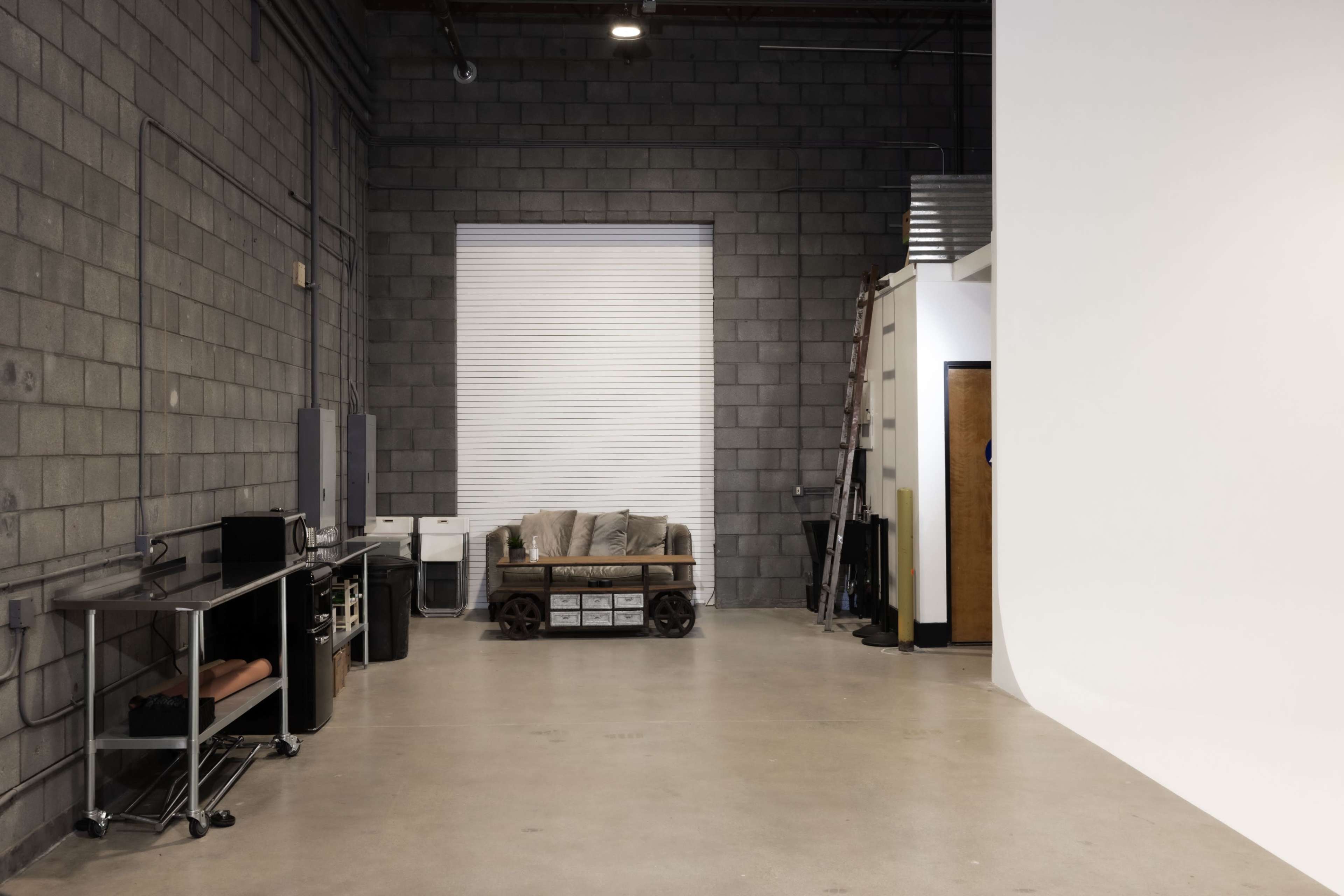 The image shows an industrial-style room with a concrete block wall, a couch on a wooden pallet, and various furniture pieces along one side.