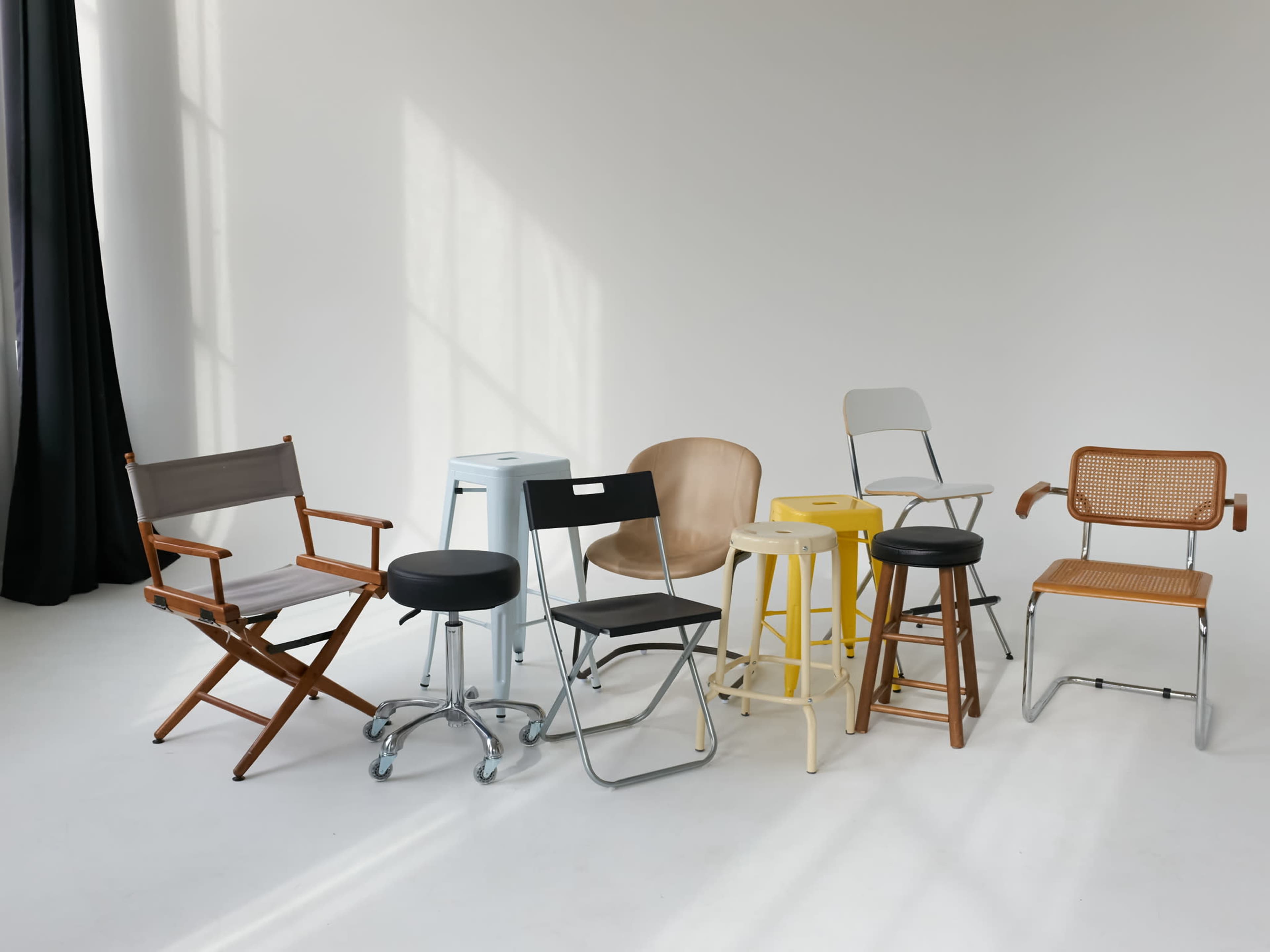 The image features a collection of diverse chairs arranged in a semi-circle against a plain backdrop.