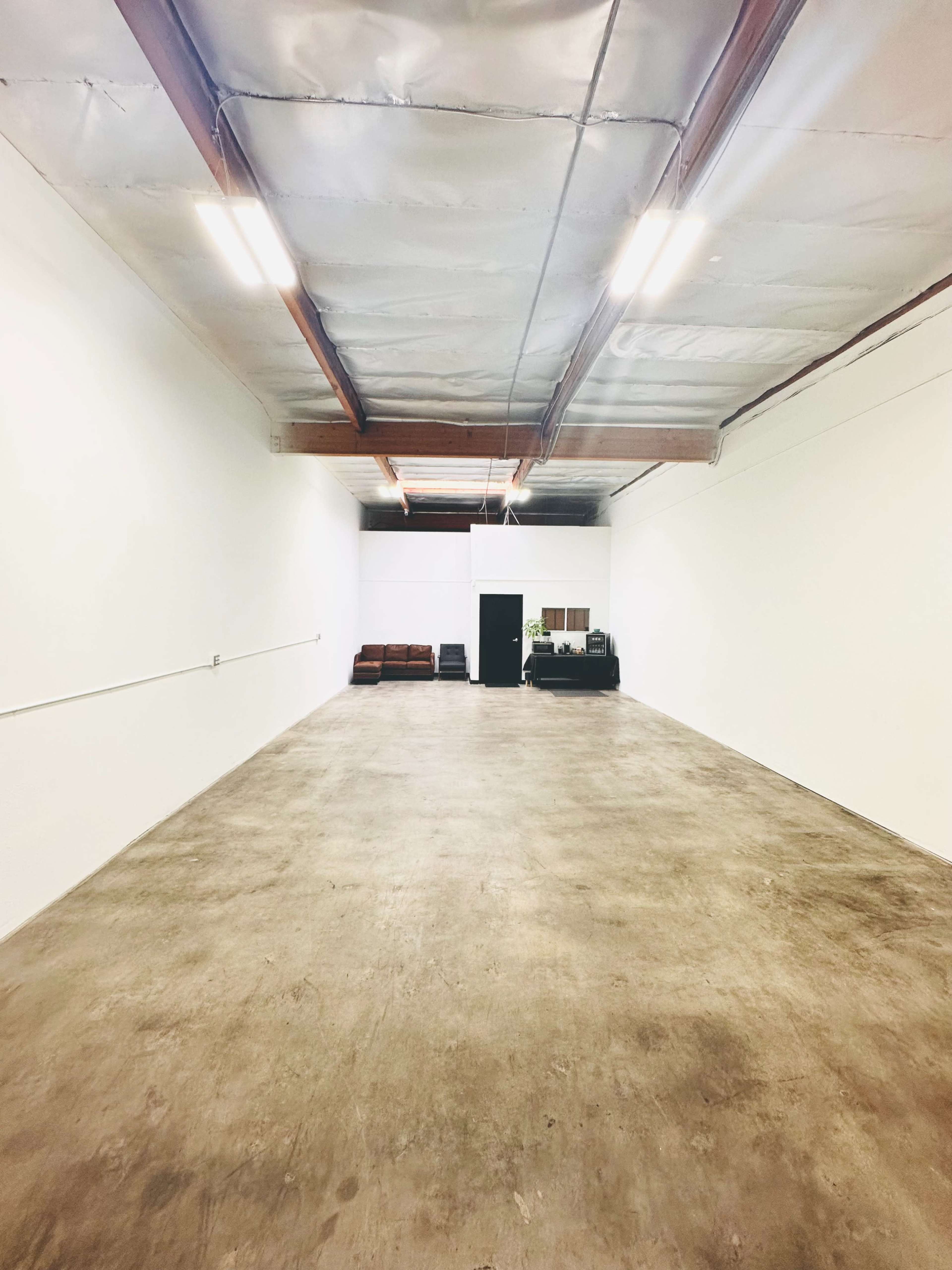 A large, empty industrial space with a concrete floor, white walls, and exposed ceiling beams.