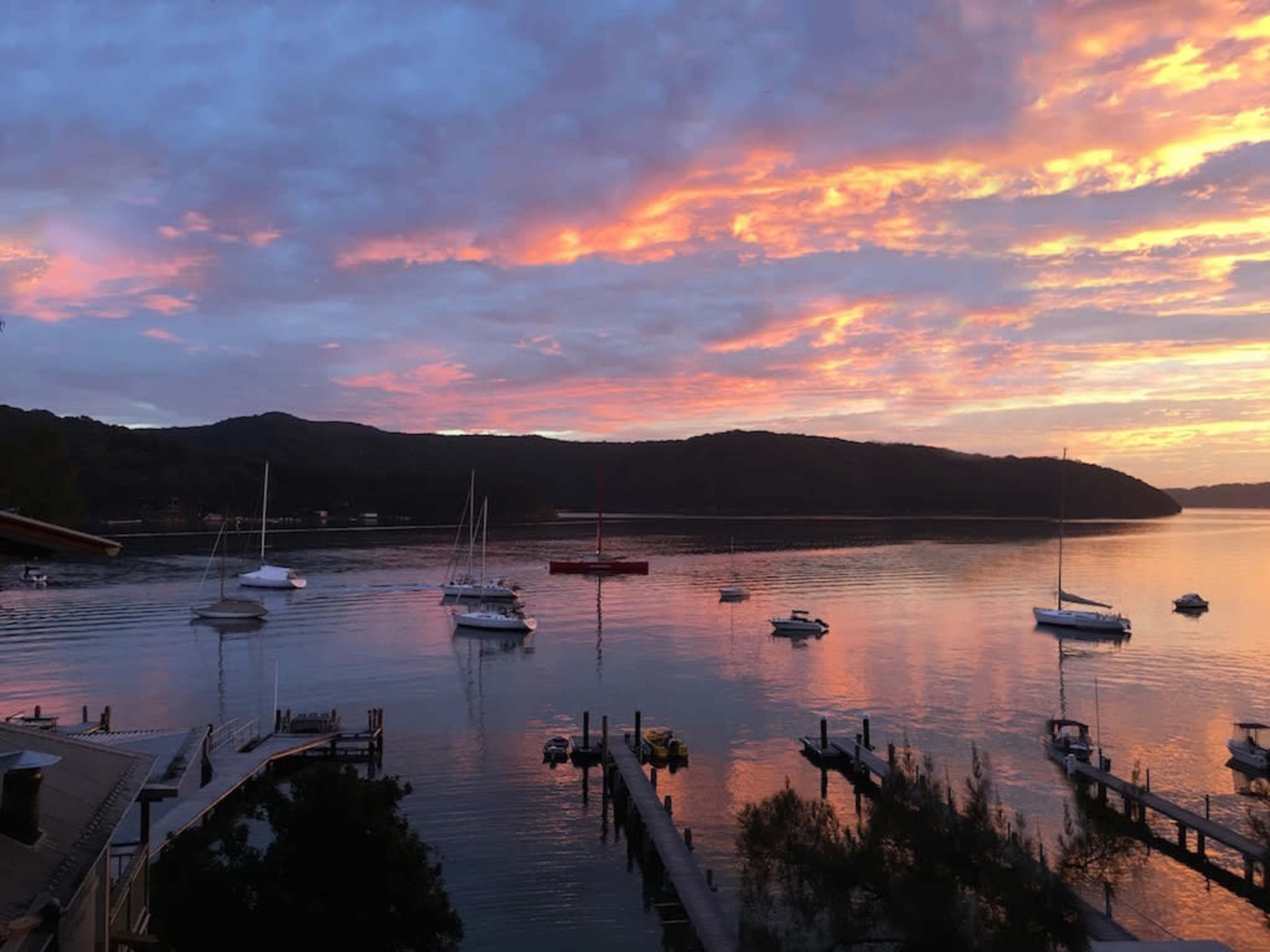 The scene captures a tranquil lake at sunset, with several boats anchored and vibrant colors reflected in the water.