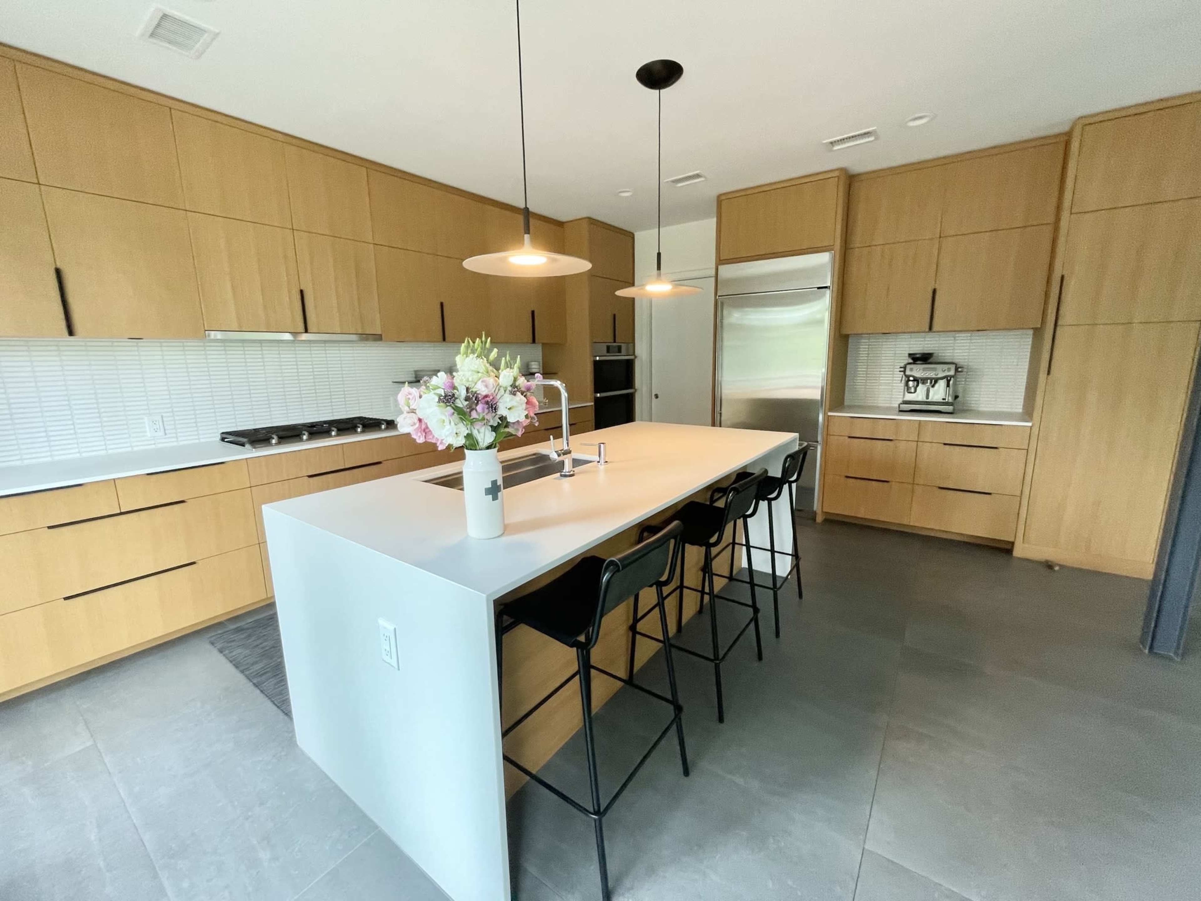 A modern kitchen features wooden cabinetry, a central island with seating, and pendant lighting above.