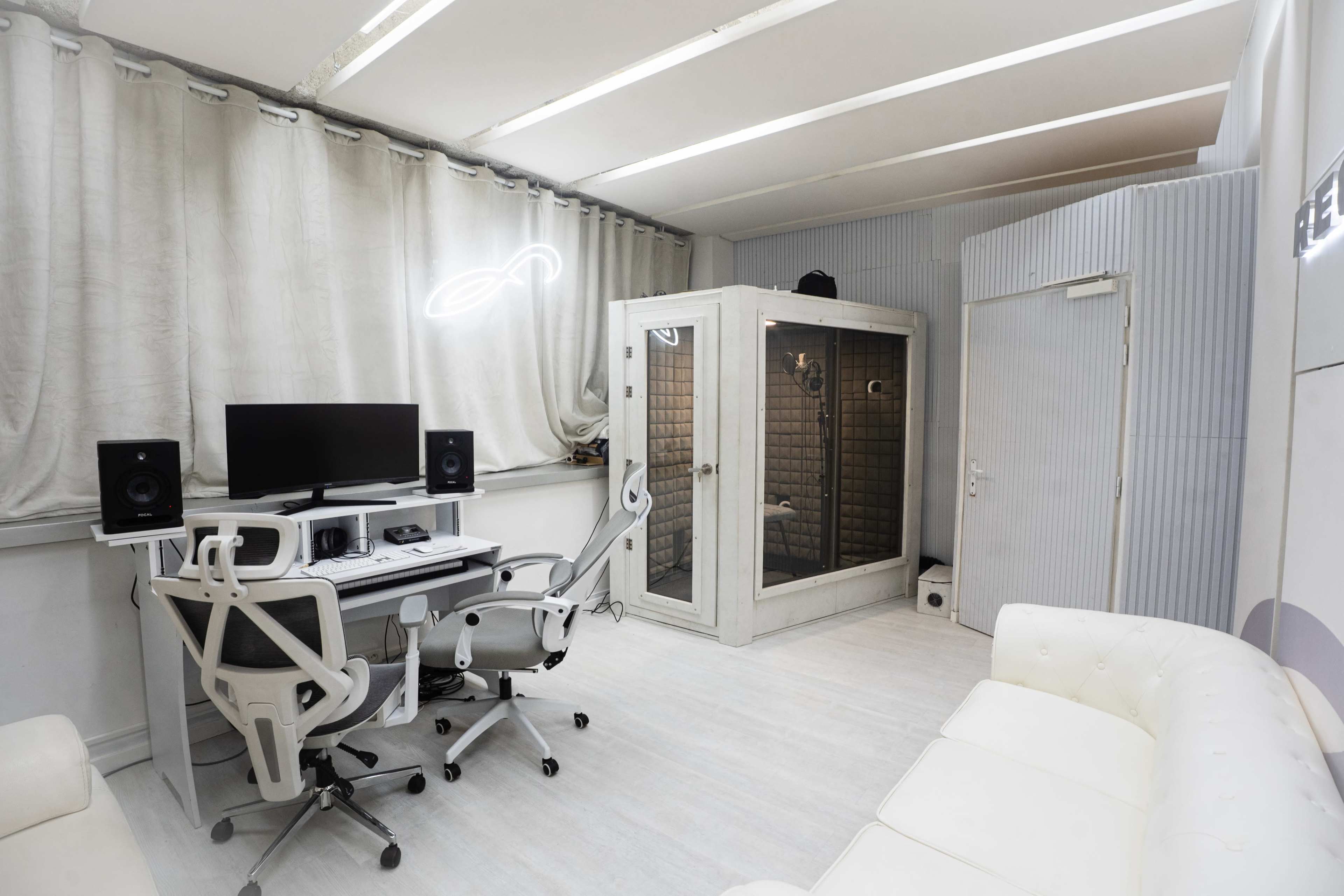 The room features a modern workspace with a desk, computer, and speakers, along with a soundproof booth and a white couch.