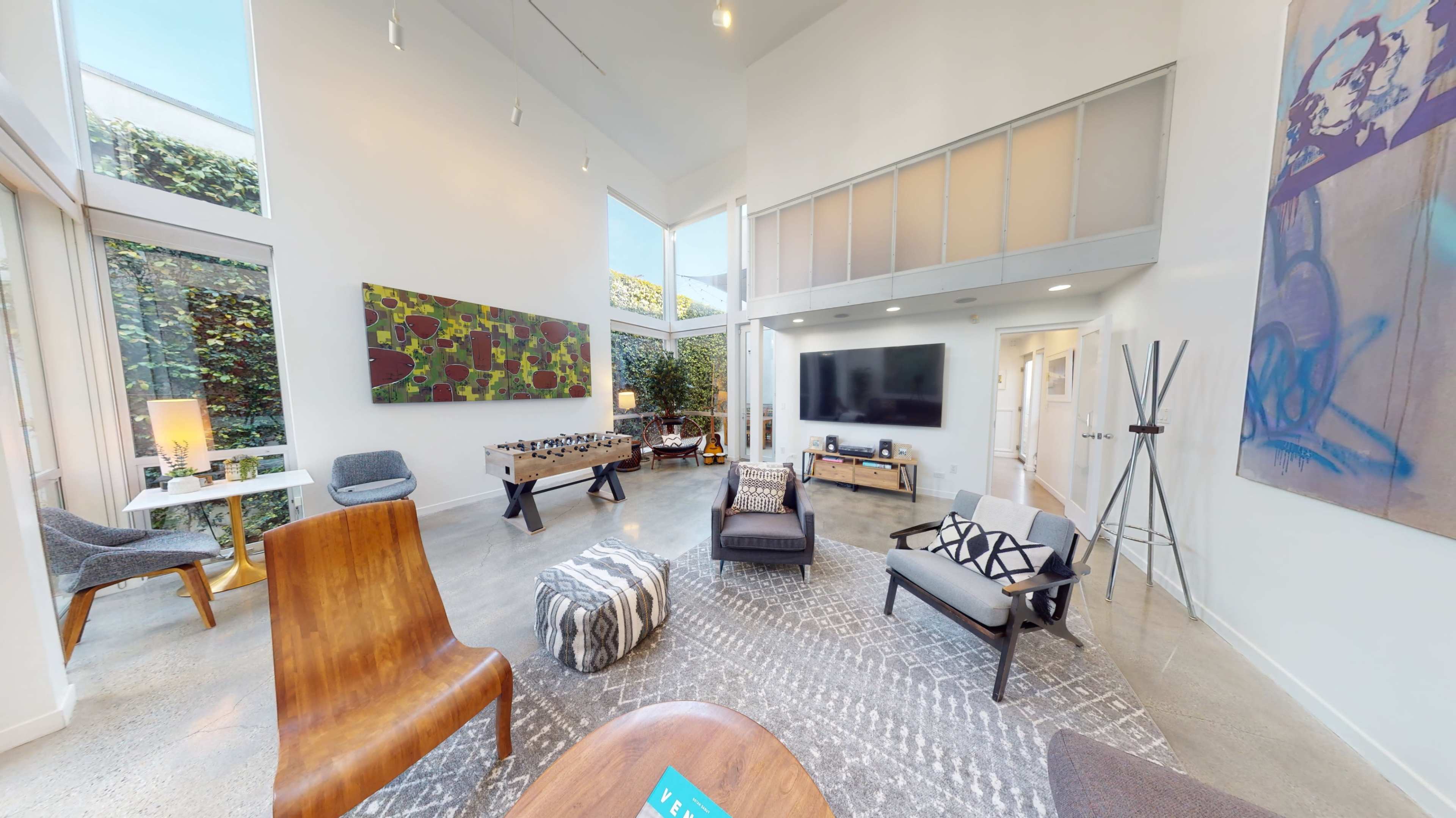 A modern, well-lit living room featuring a mix of seating options, a large television, and artistic wall decor.