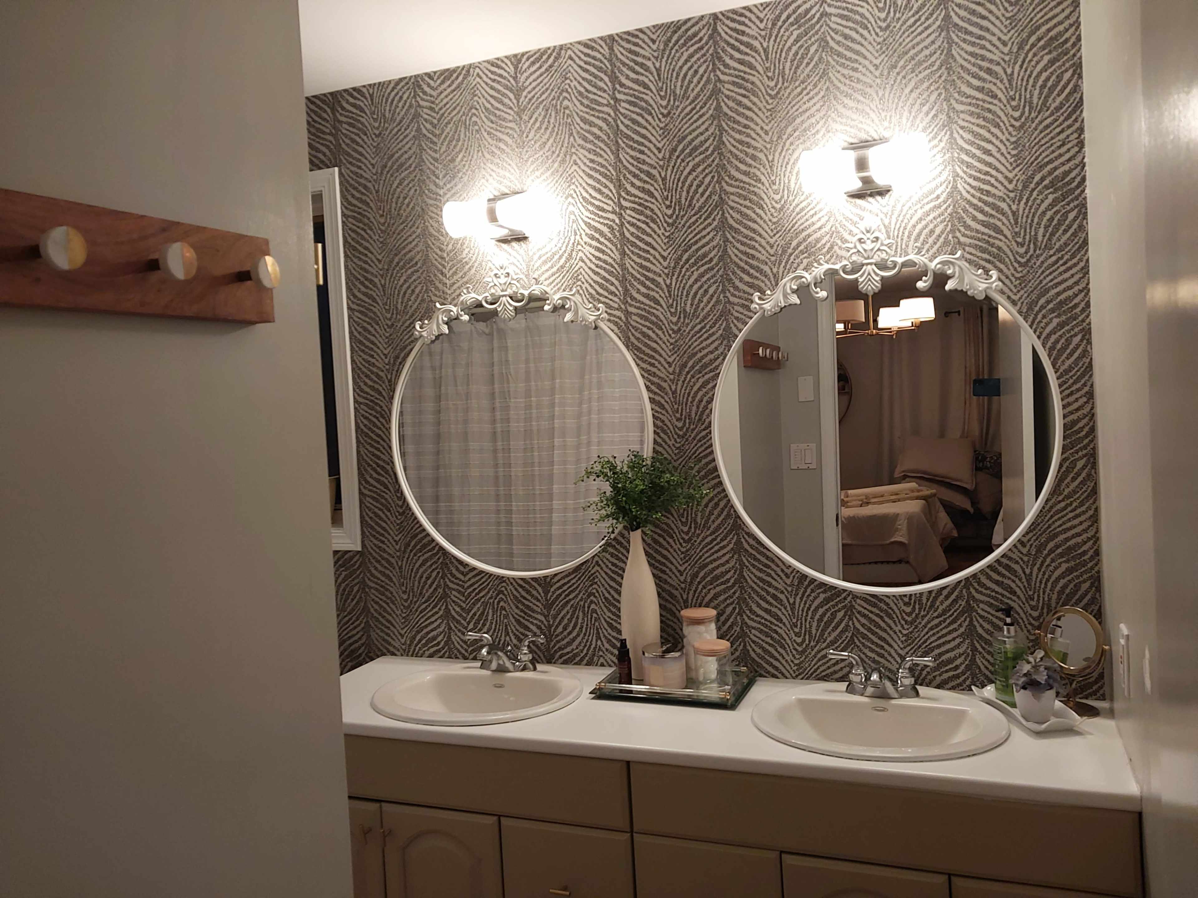 A bathroom with two circular mirrors above a double sink, featuring a patterned wallpaper and stylish light fixtures.