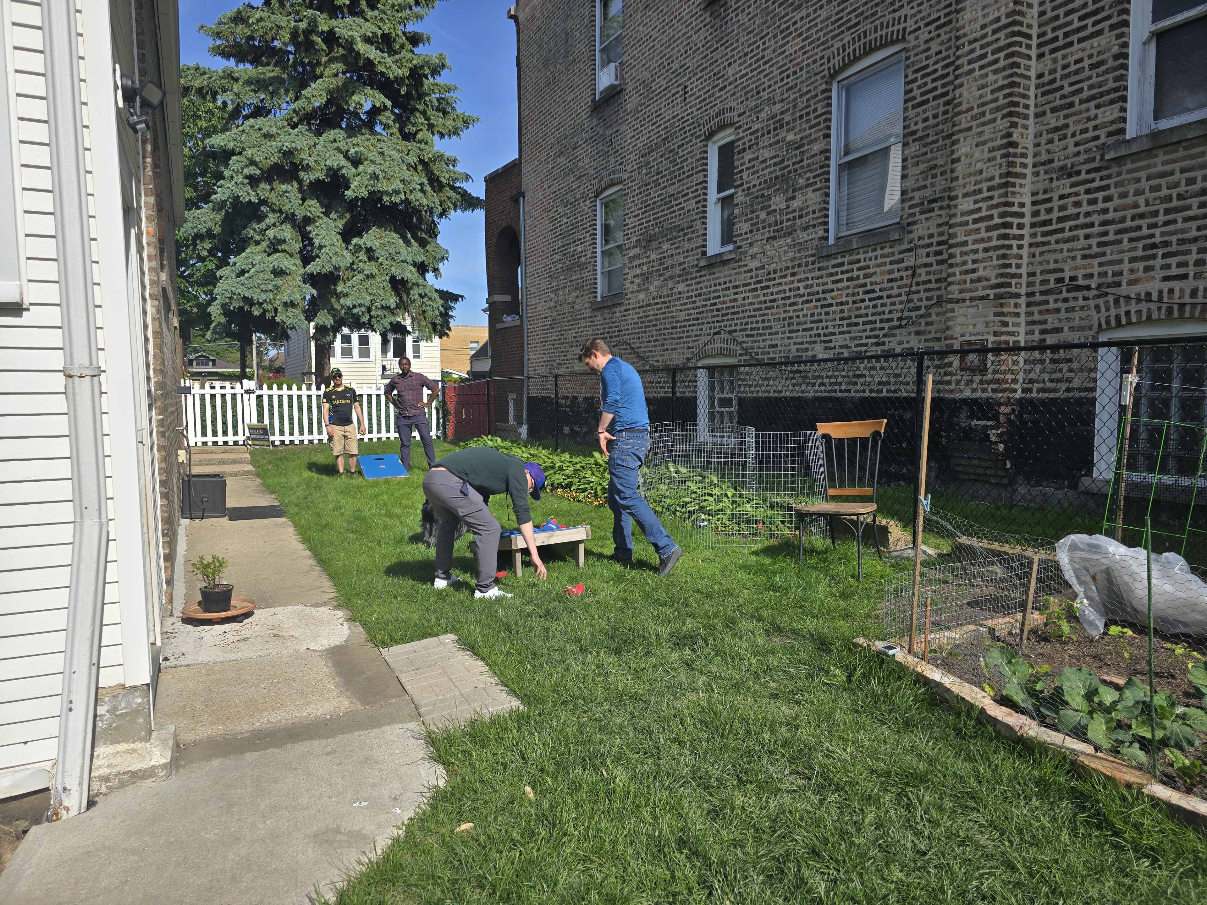 Several people are working in a backyard garden, with one person tending to plants, while others assist nearby.