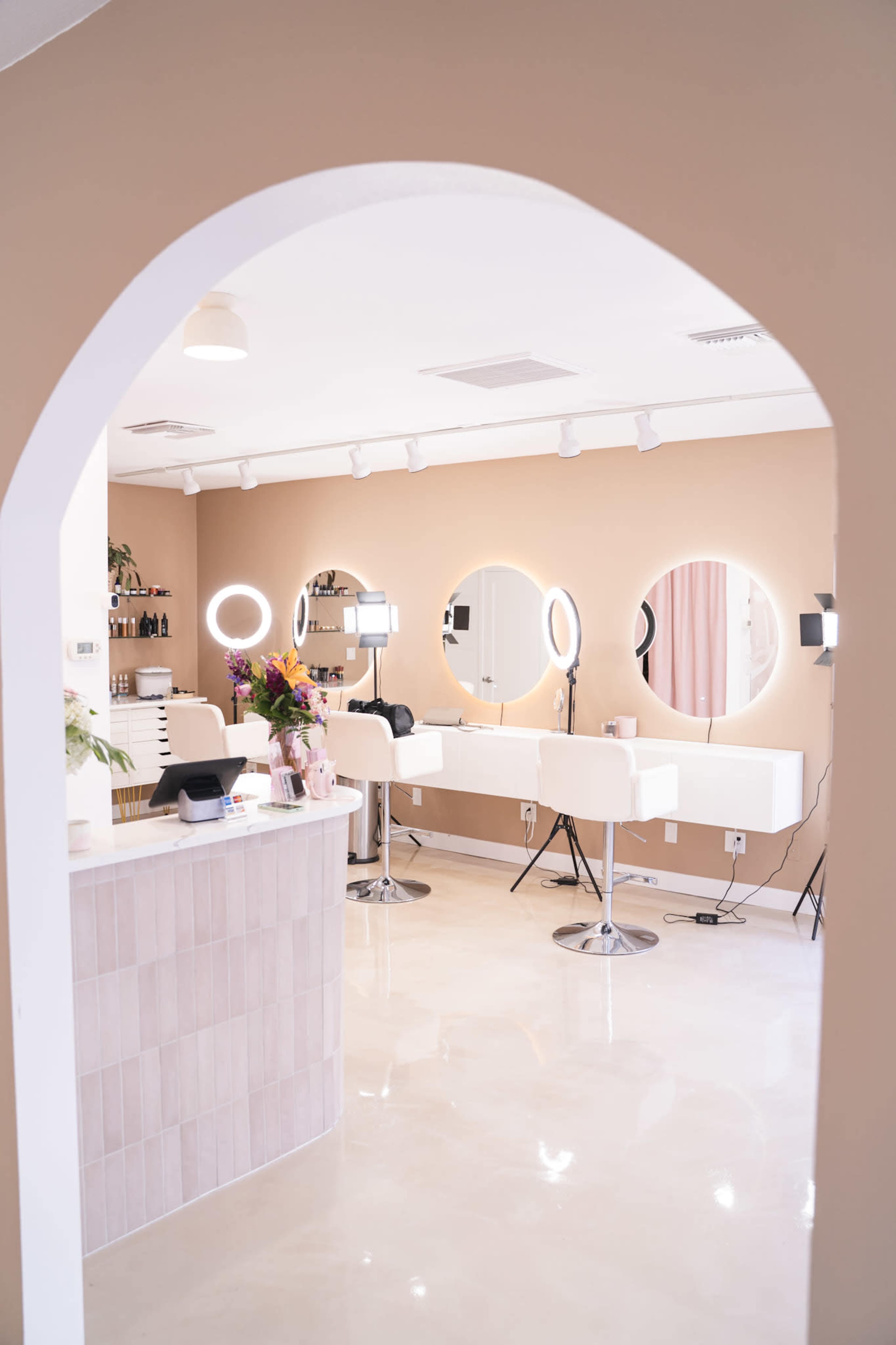A modern hair salon with illuminated round mirrors, white styling chairs, and a reception counter under an arched doorway.
