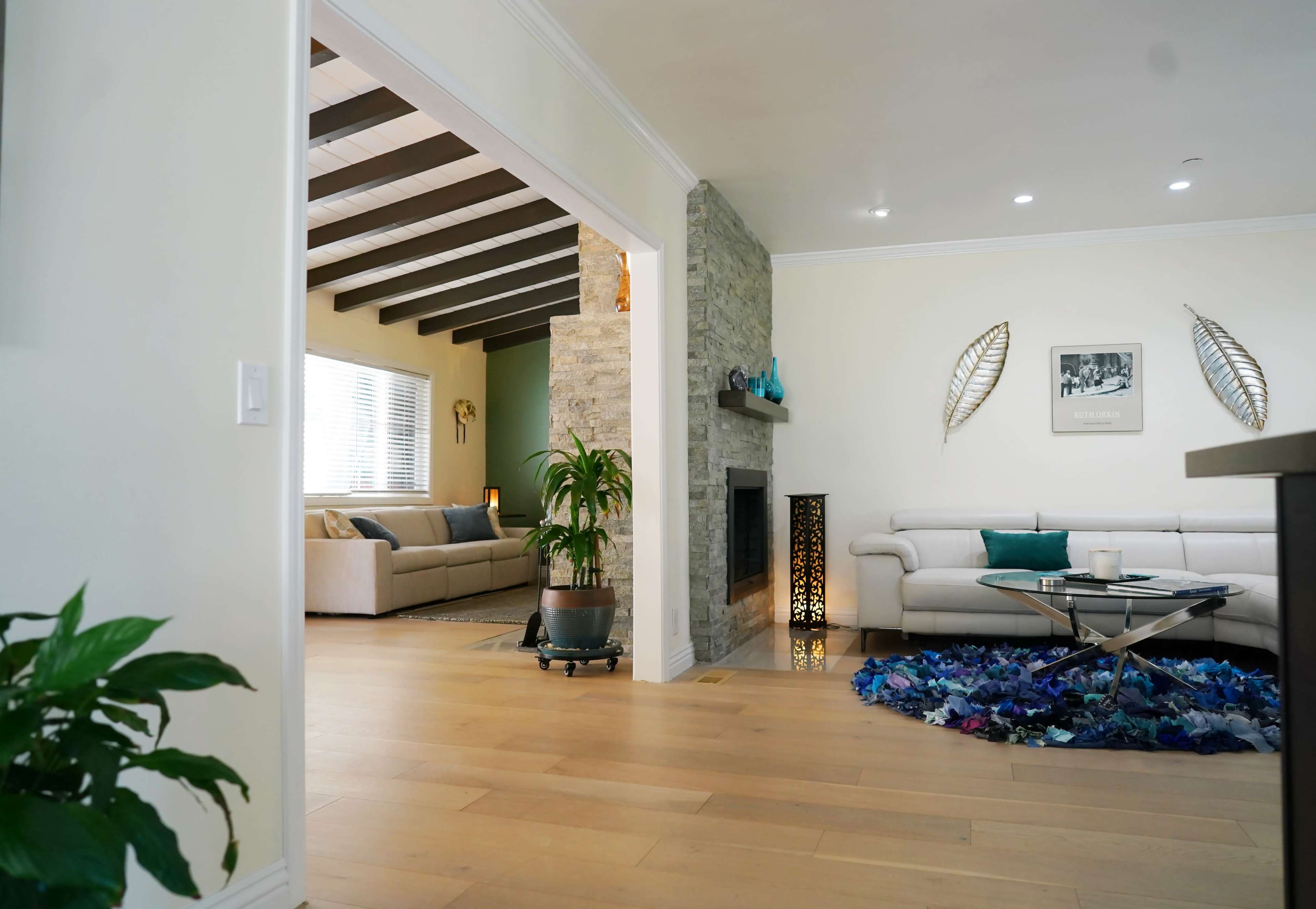 A modern living space features a light-colored room with a stone fireplace, a cozy sofa, and decorative elements like a plant and a unique textile rug.