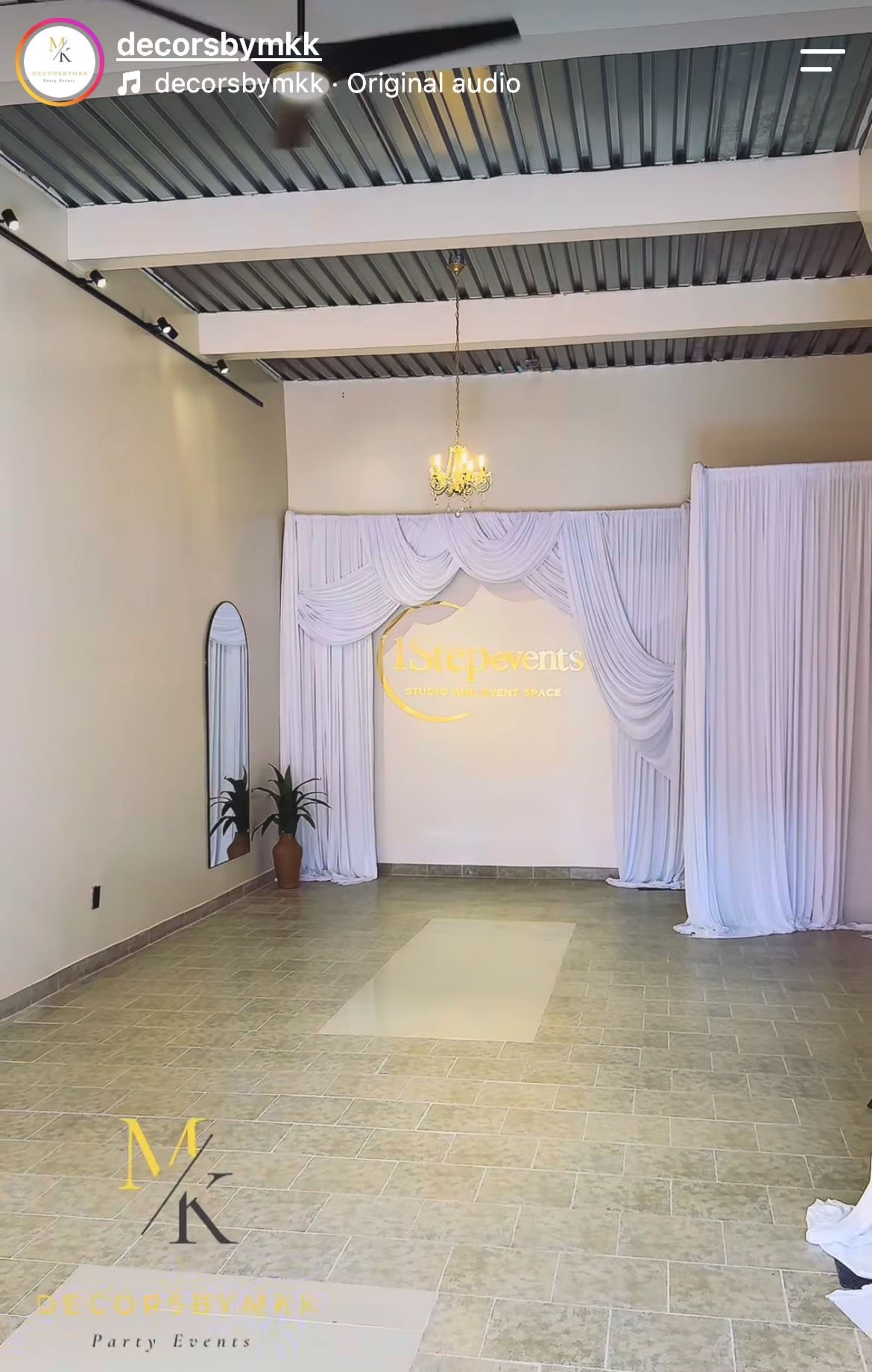 The image shows an event space with light-colored walls, a decorative chandelier, and draped fabric along one side.