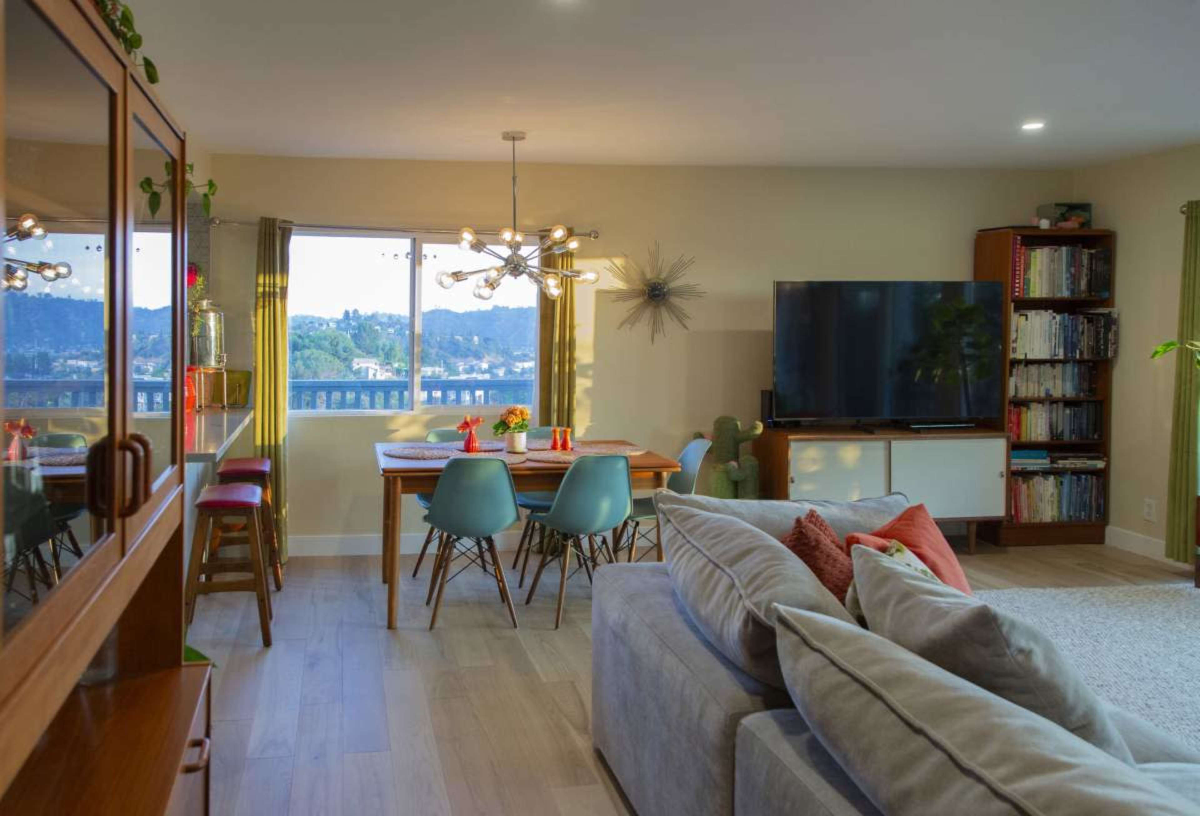 A modern living area features a sofa, dining table with chairs, and a television, all set against a backdrop of a scenic view through large windows.