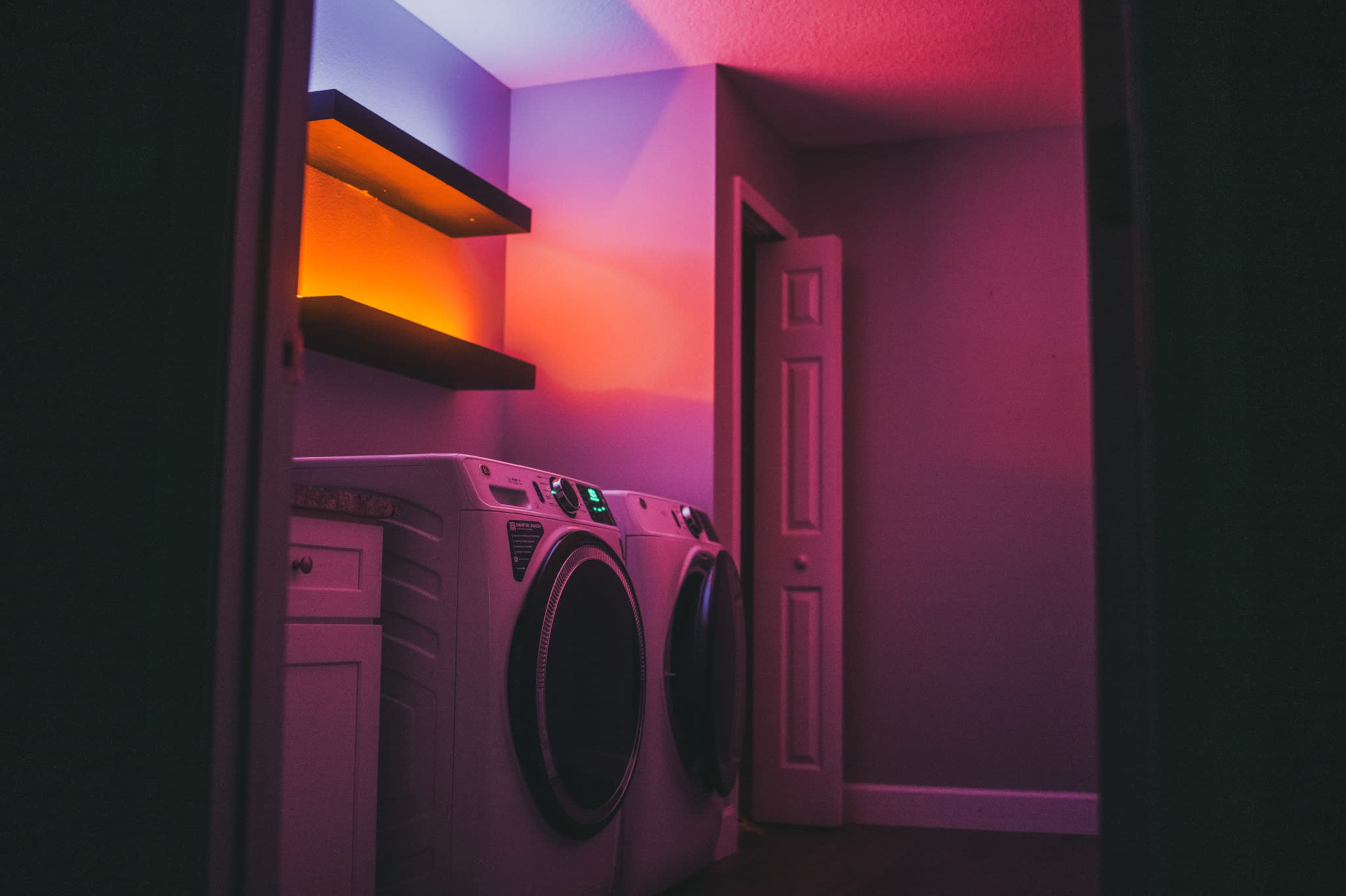 A laundry room features two white washing machines and a shelf illuminated with colorful lights.