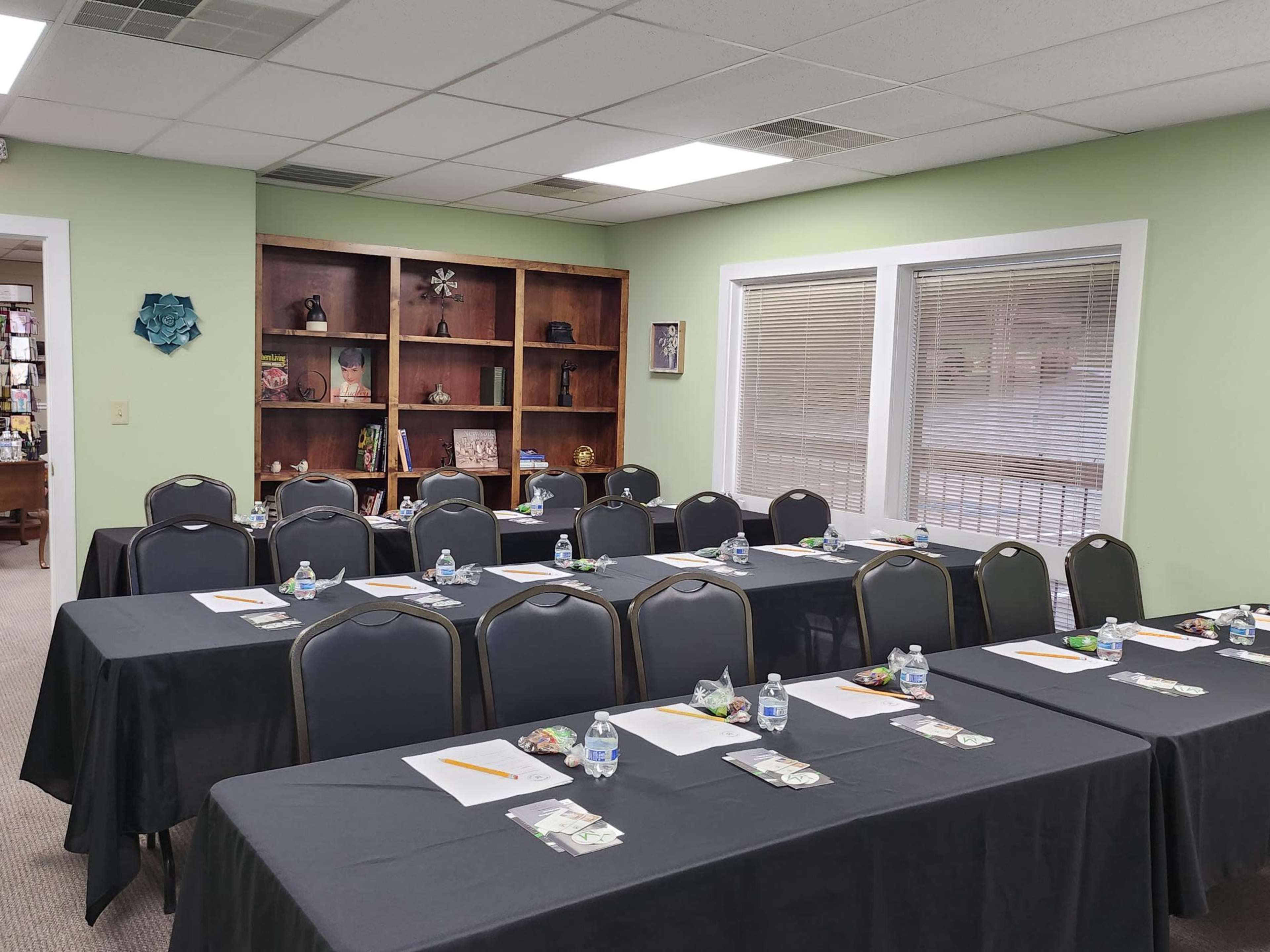 A classroom or meeting room set up with several tables covered in black cloth, each equipped with a water bottle, snacks, and writing materials.