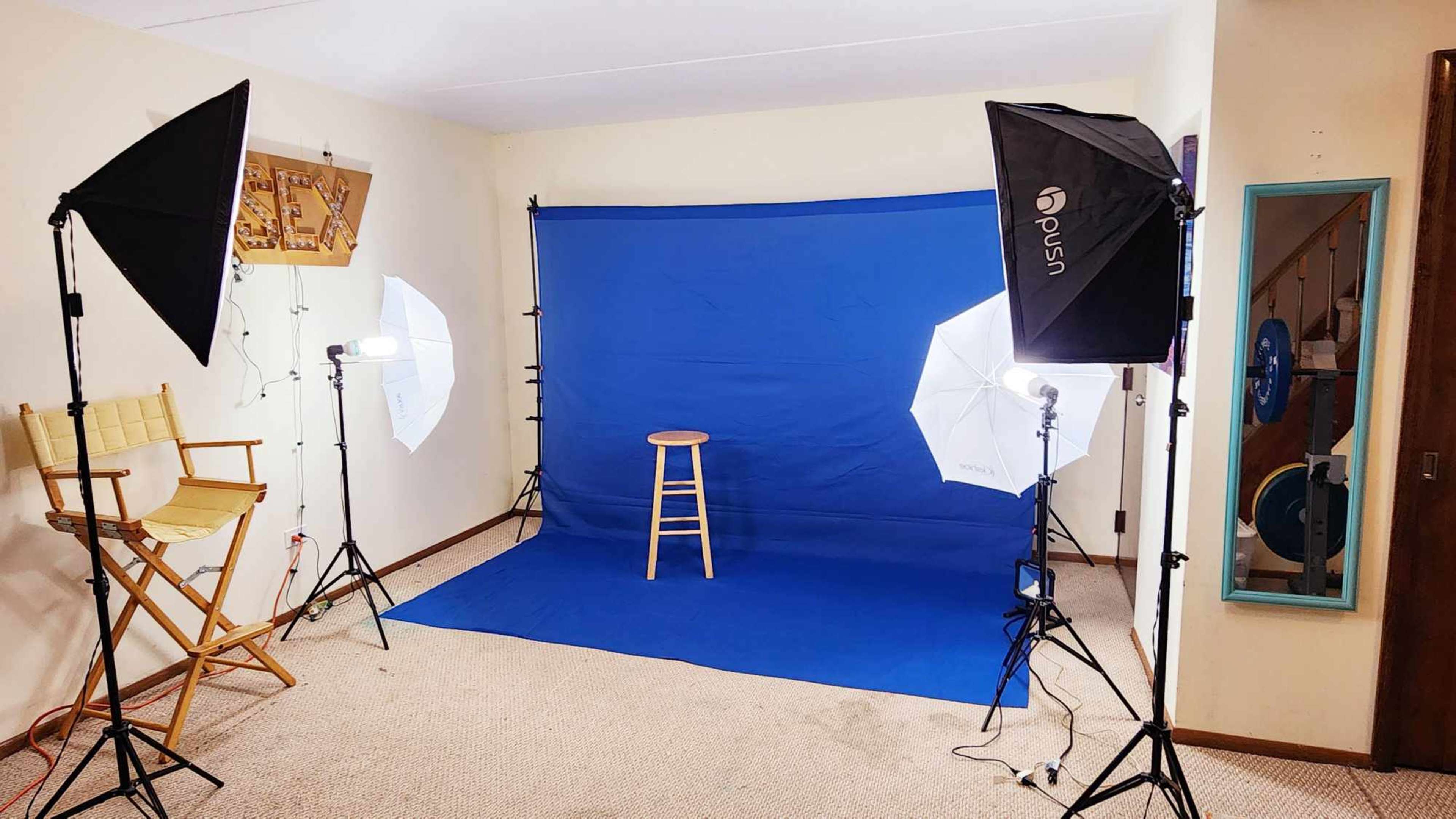 A photography setup with a blue backdrop, a wooden stool, and multiple studio lights arranged around the scene in a room with carpeted flooring.
