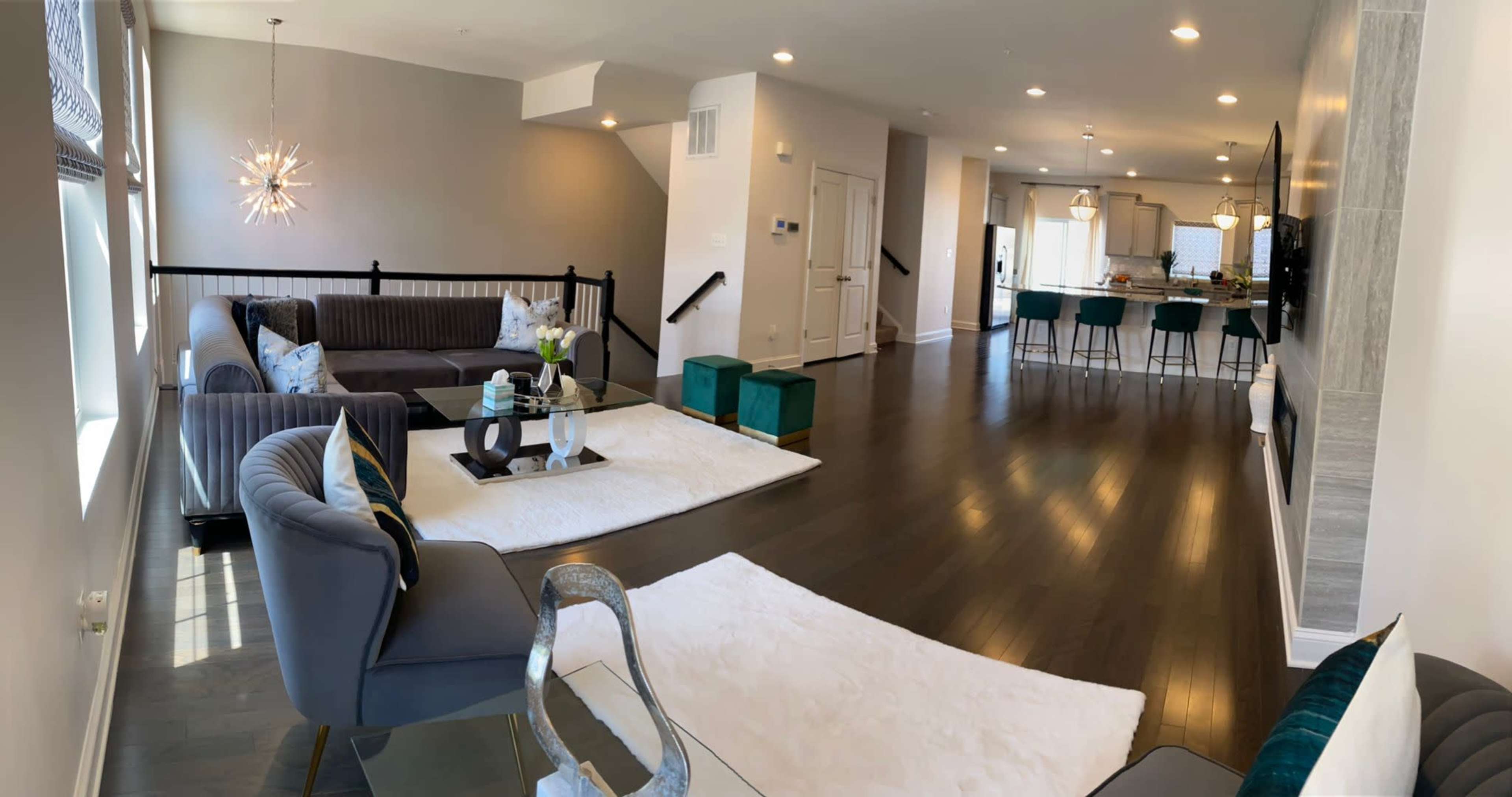 A spacious living room with modern furniture, including a sectional couch and armchairs, leading to an open kitchen area with bar seating.