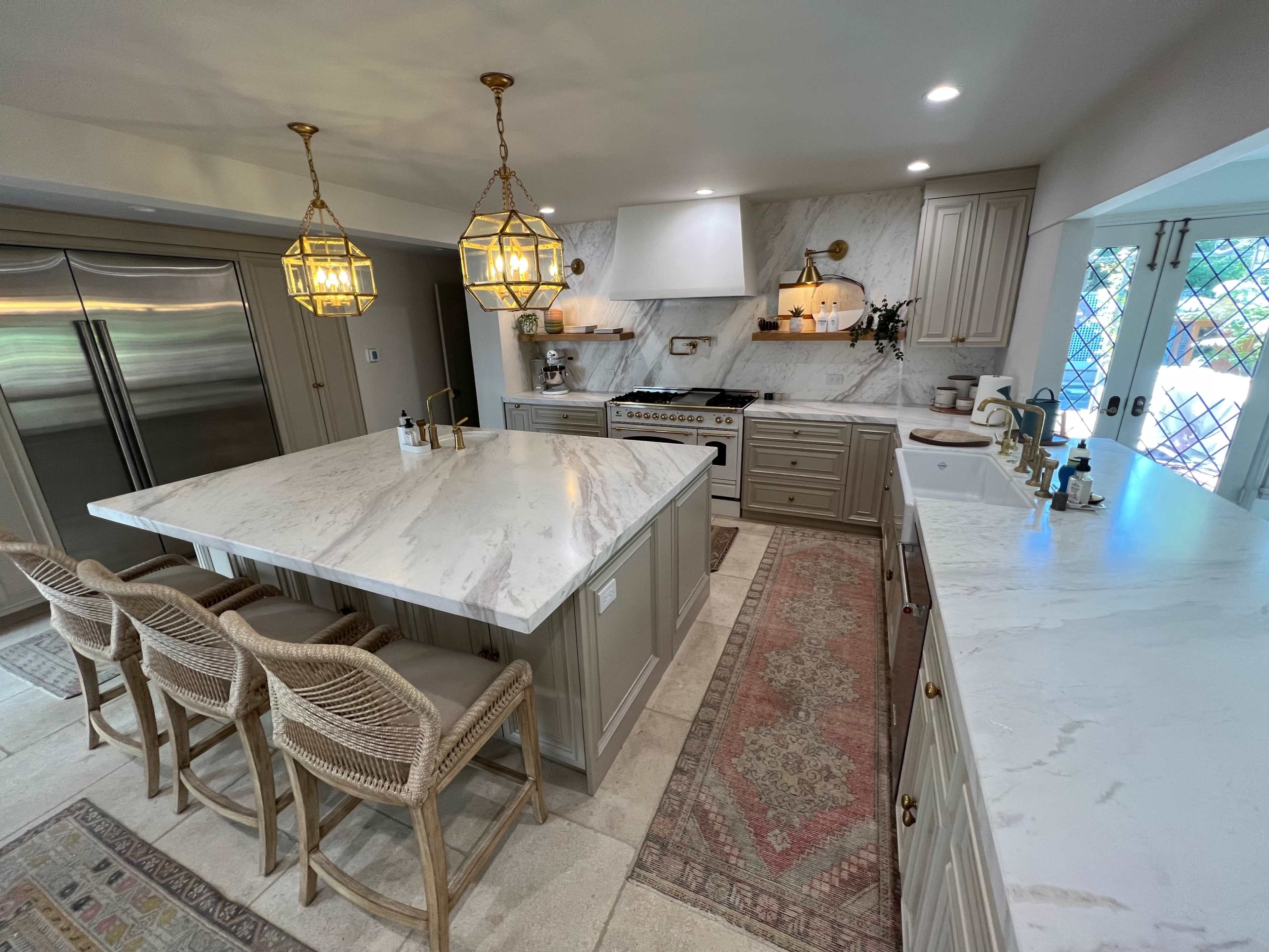 The kitchen features a large marble island, modern appliances, and pendant lights, with bar seating along one side.