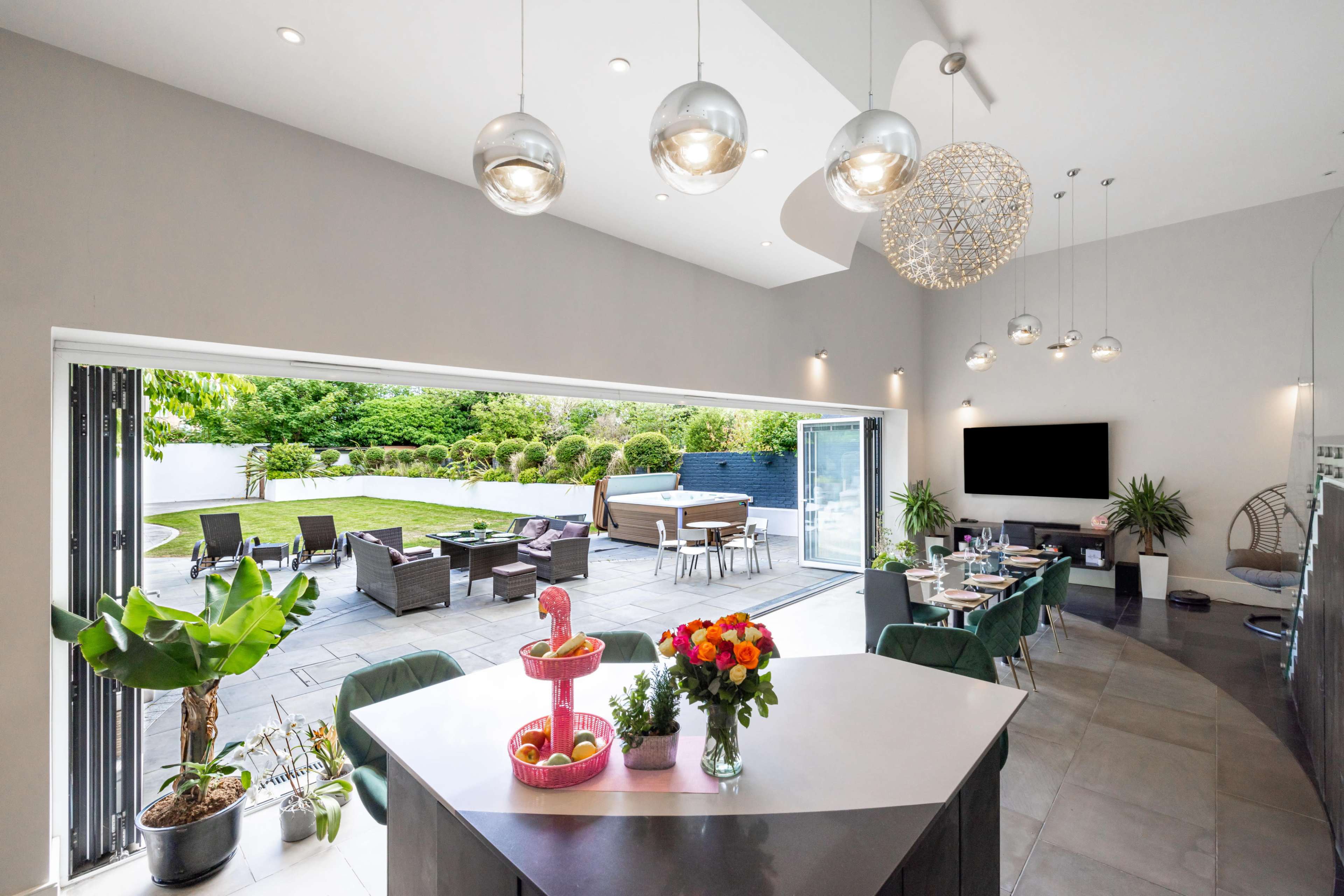 A modern kitchen with a central island overlooks a spacious outdoor patio and garden through wide sliding glass doors.