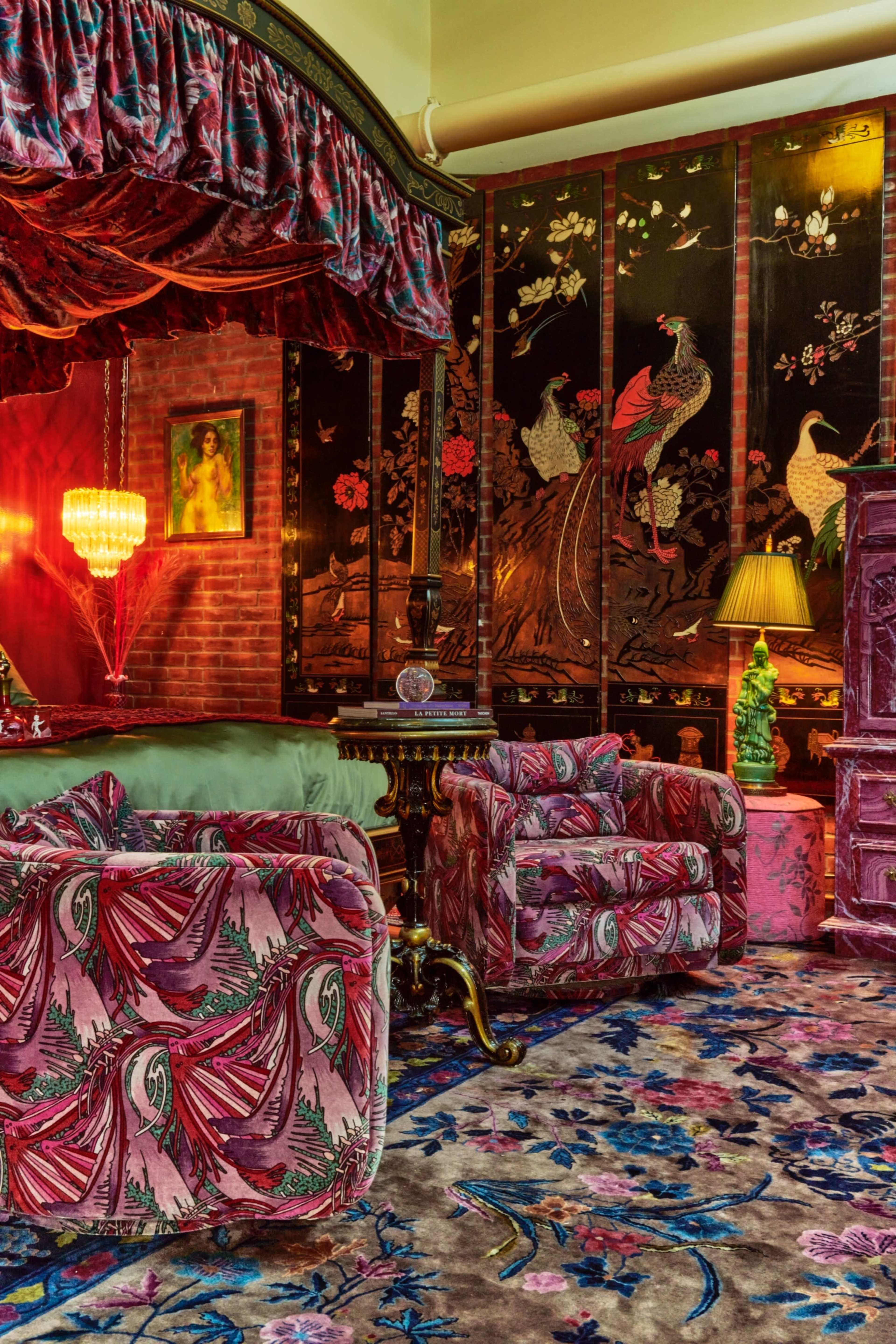 A richly decorated living room with patterned upholstery, floral wallpaper, and intricate wooden panels featuring peacock designs.