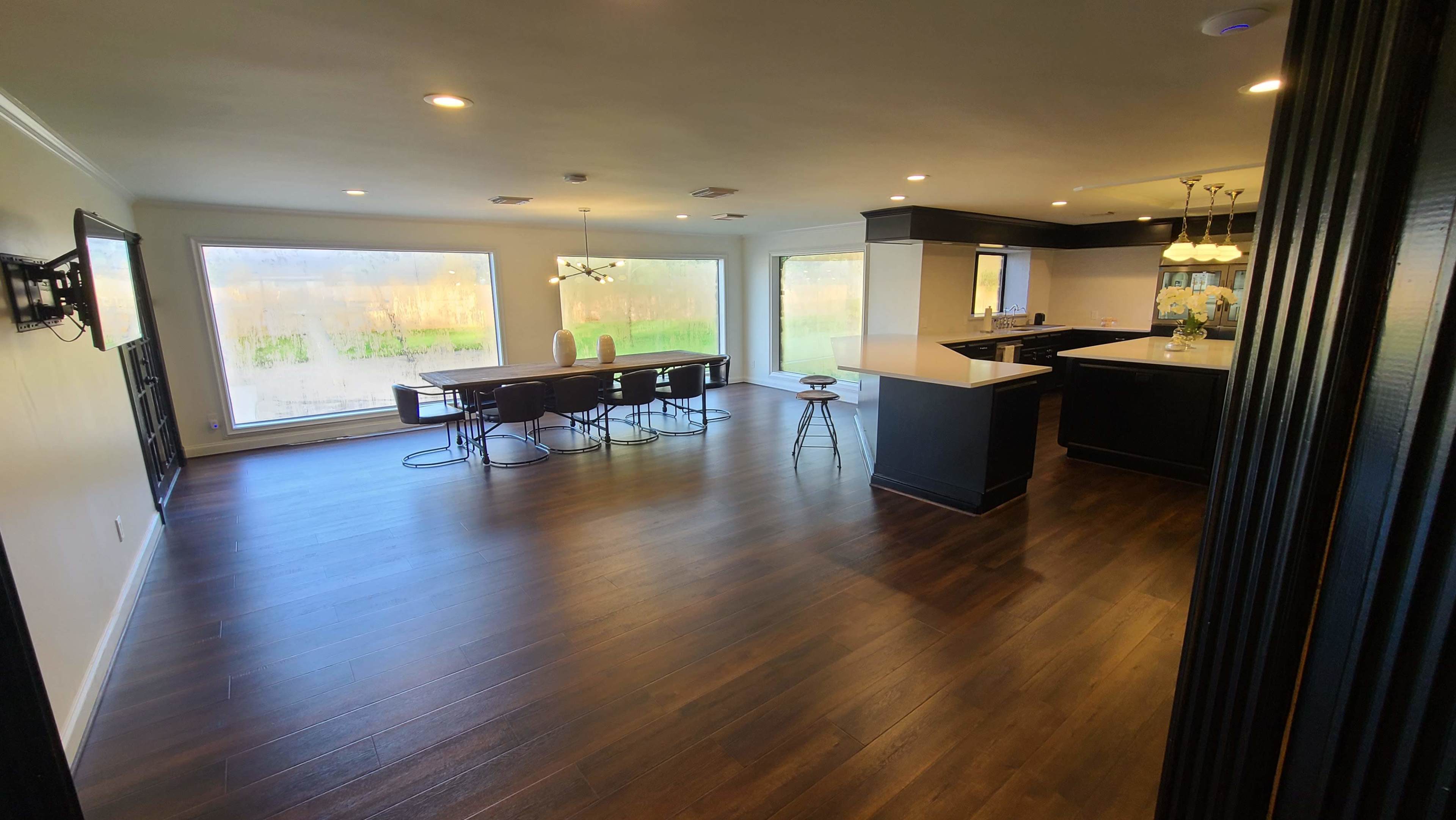 The image shows a spacious modern kitchen and dining area with large windows overlooking an outdoor space.