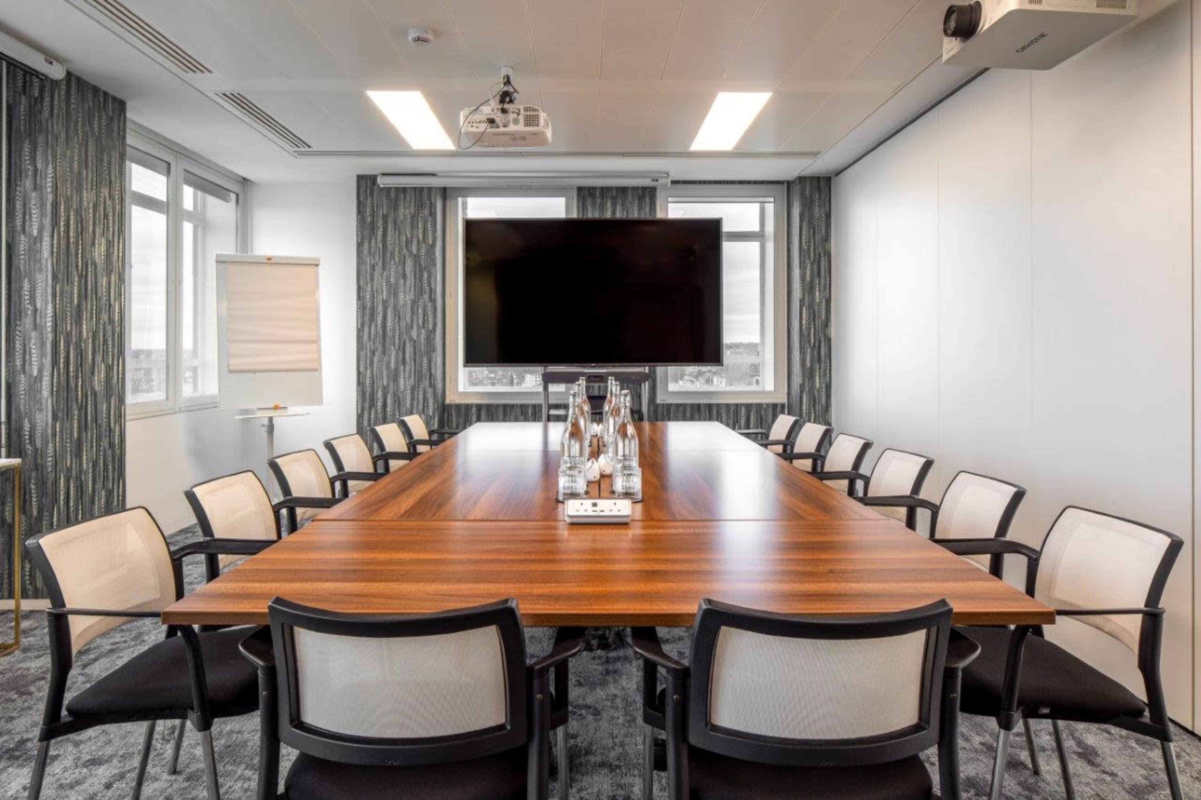 A large conference room features a wooden table surrounded by chairs, a projector, and a large screen on the wall.