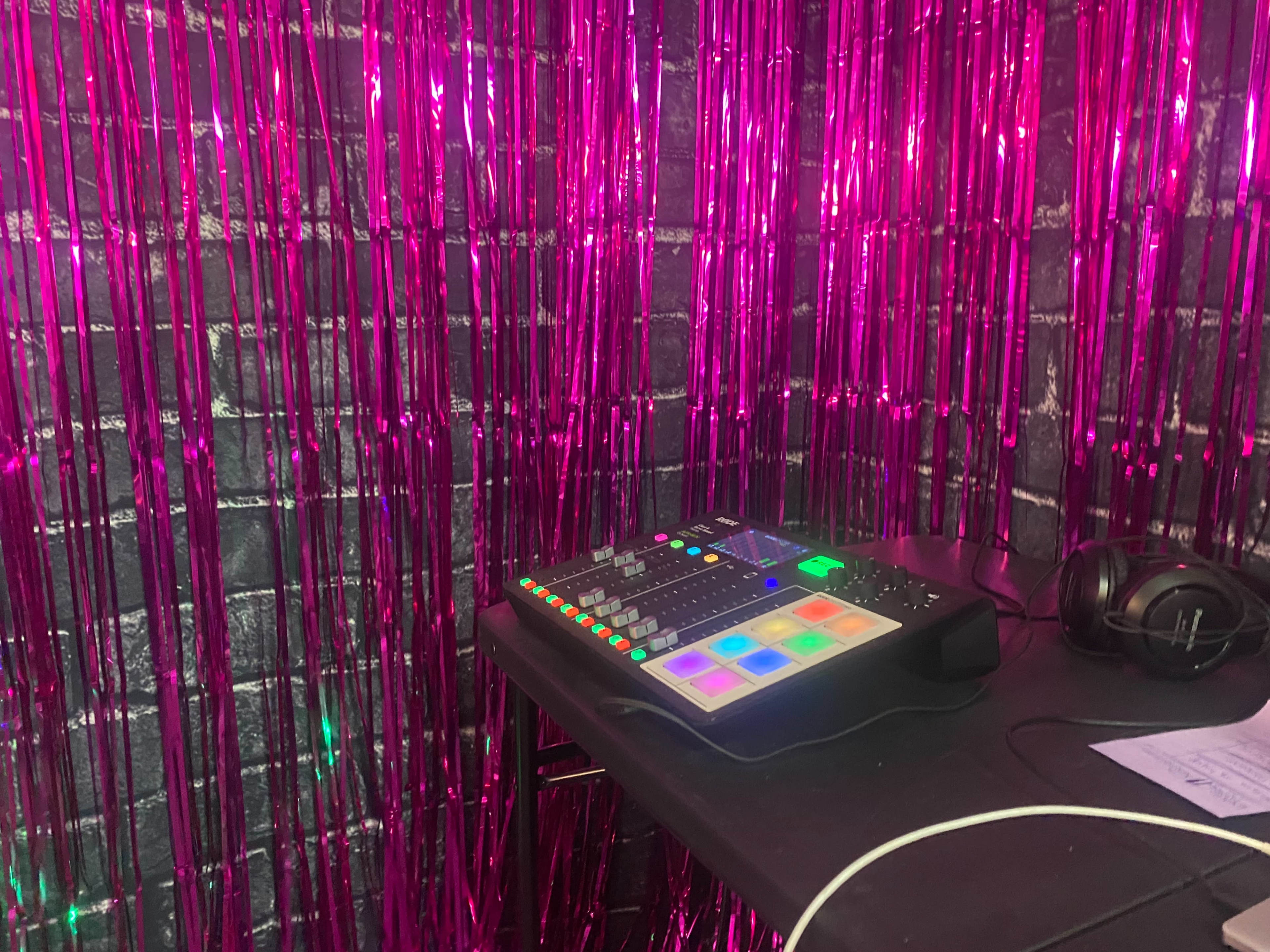 A music production setup is placed on a table against a backdrop of shiny pink streamers.