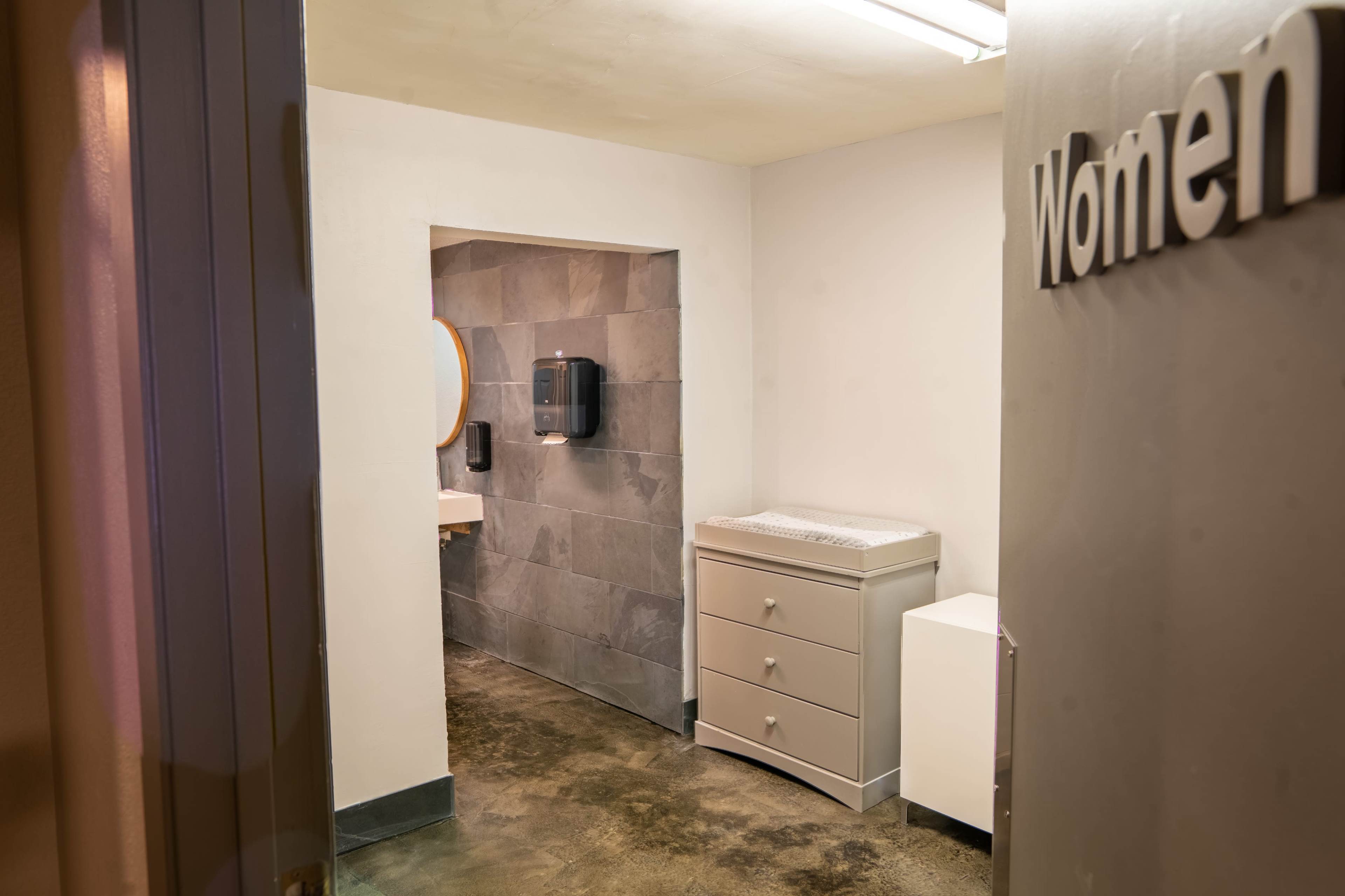 A restroom entrance labeled "Women," with a narrow hallway leading to a sink area and cabinets.