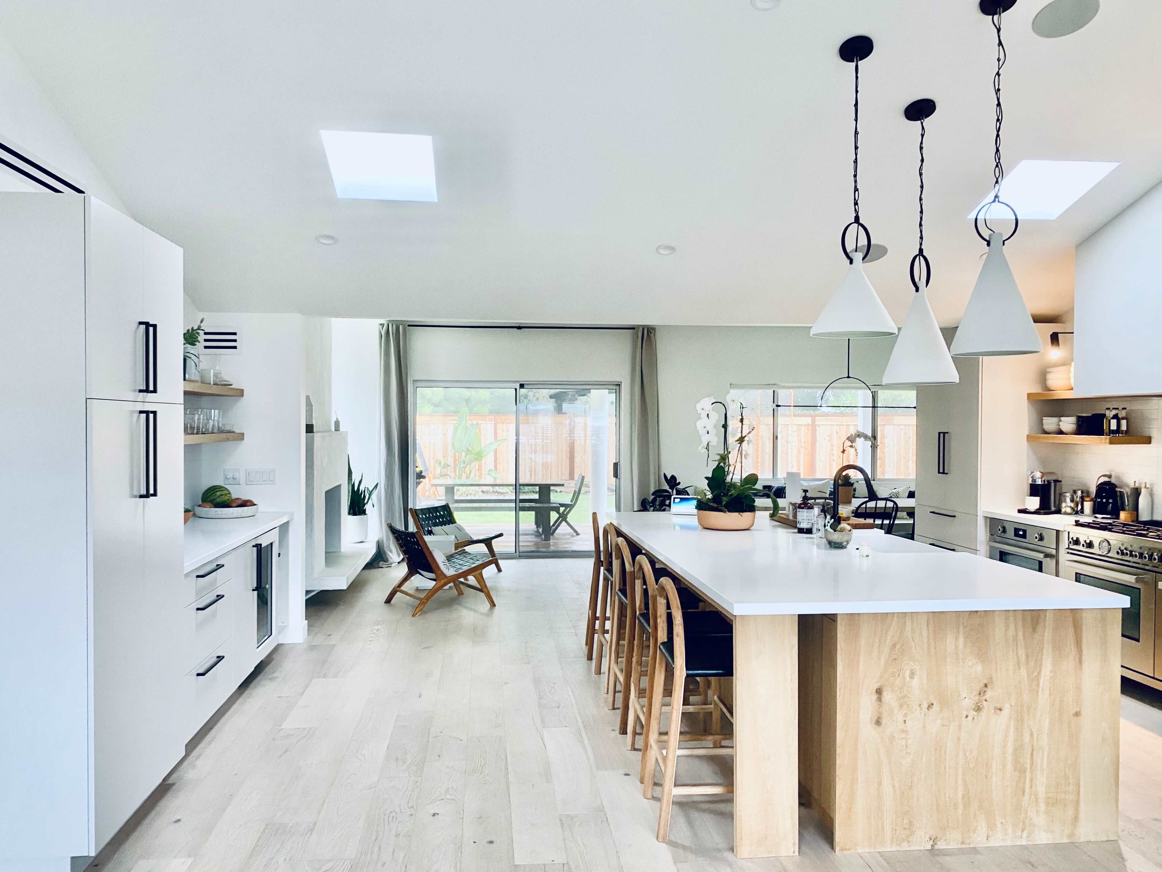 The kitchen features a central island with wooden accents, pendant lighting, and an open layout leading to a patio area.