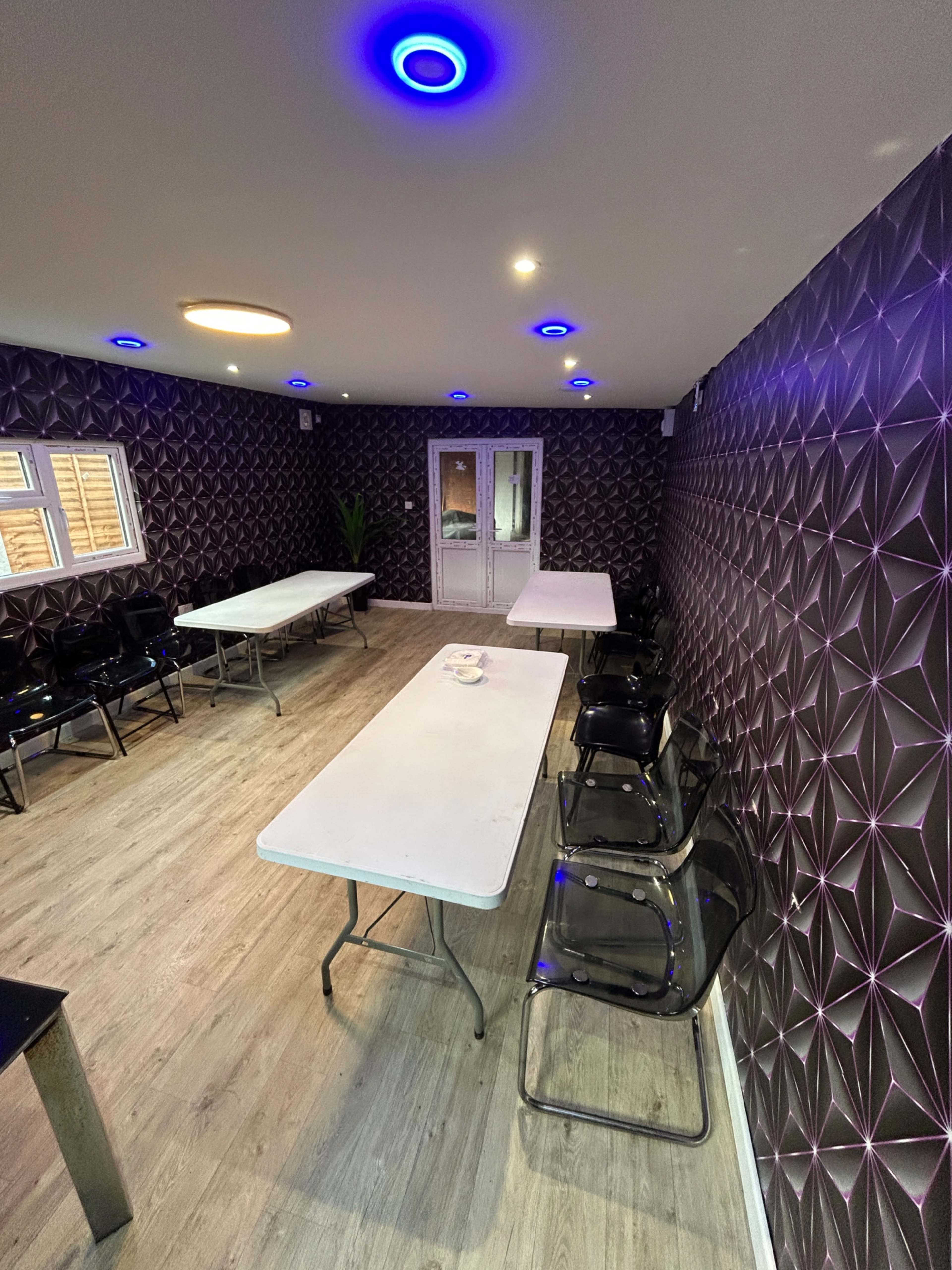 The room features multiple tables and chairs against a patterned wall, illuminated by colorful ceiling lights.
